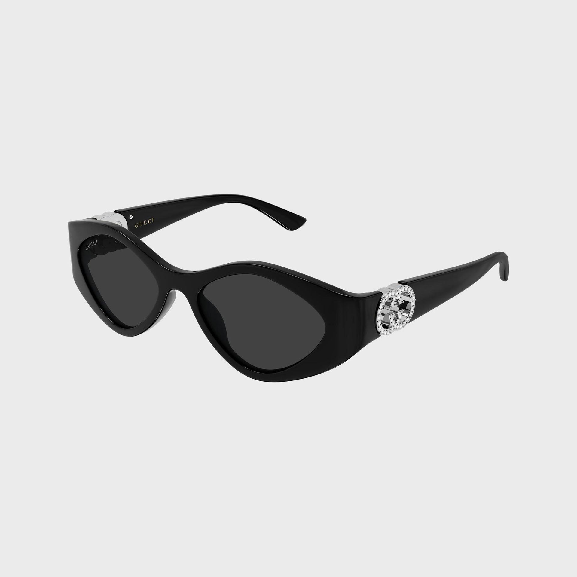 Gucci Interlocking G sunglasses, black oval frame, grey lenses, 3/4 view, crystal-set silver GG logo on temple