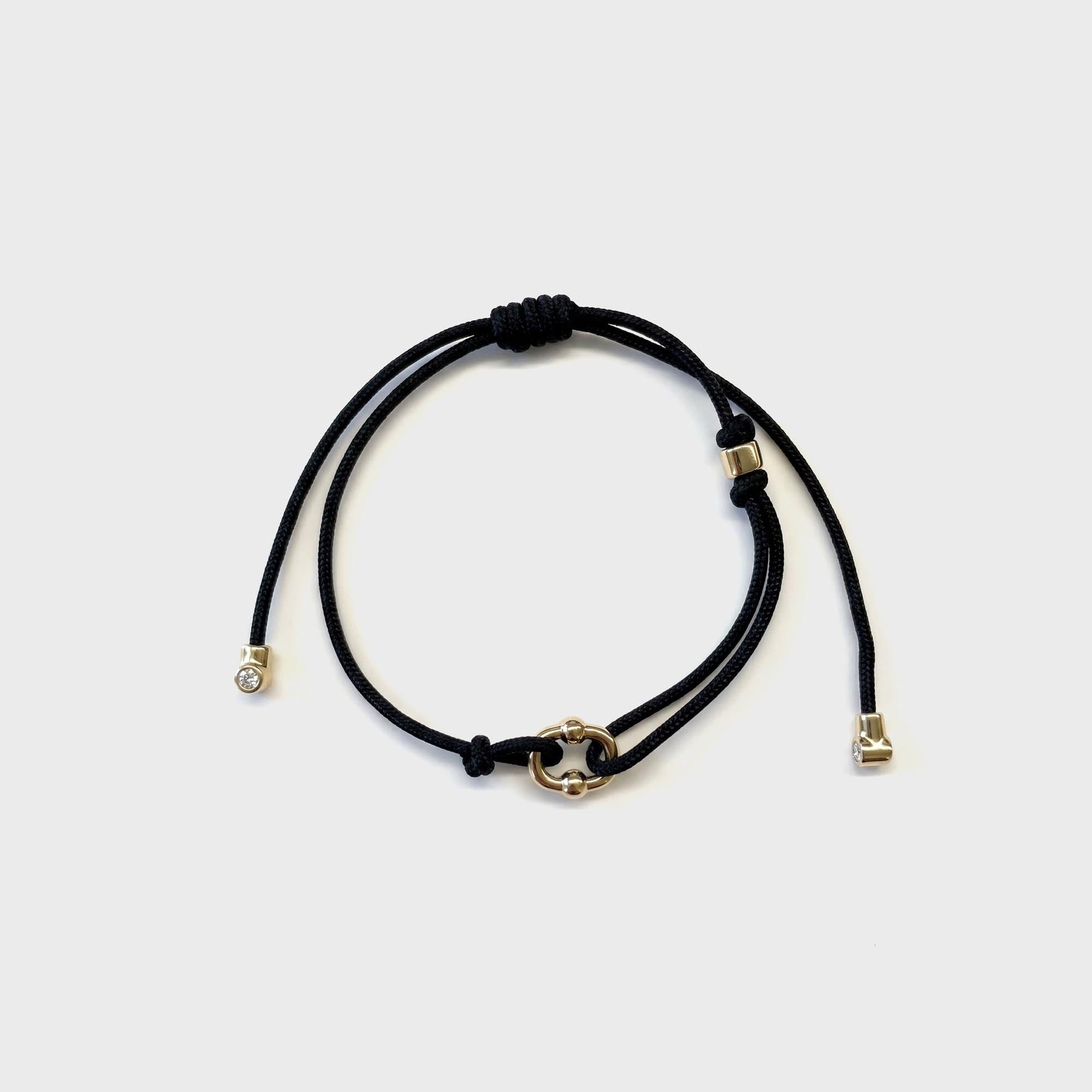 Greg Yuna Umlaut adjustable black cord bracelet with gold interlocking link charm and diamond-tip ends, flat lay