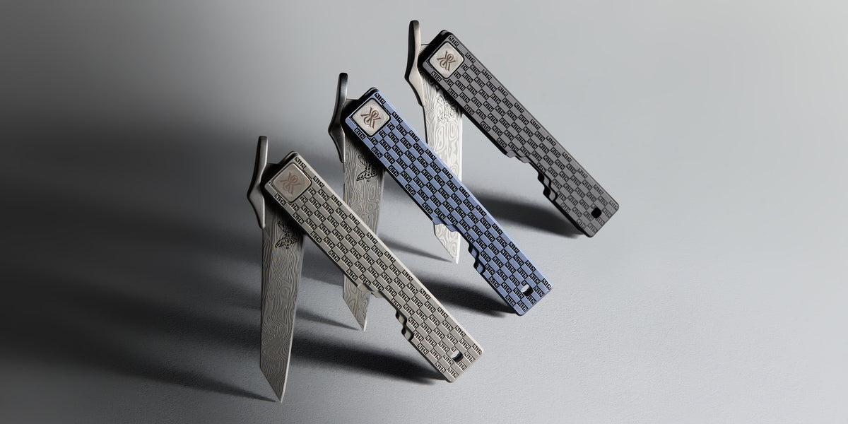 Three Kith x Benchmade folding knives with open Damascus-steel blades and KITH-monogram titanium handles in silver, blue check and grey, wide crop