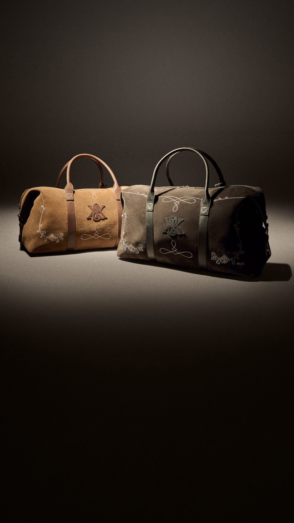 Kith suede weekender duffels in tan and taupe with embroidered monogram crest and leather trim, paired on a dark gradient studio backdrop