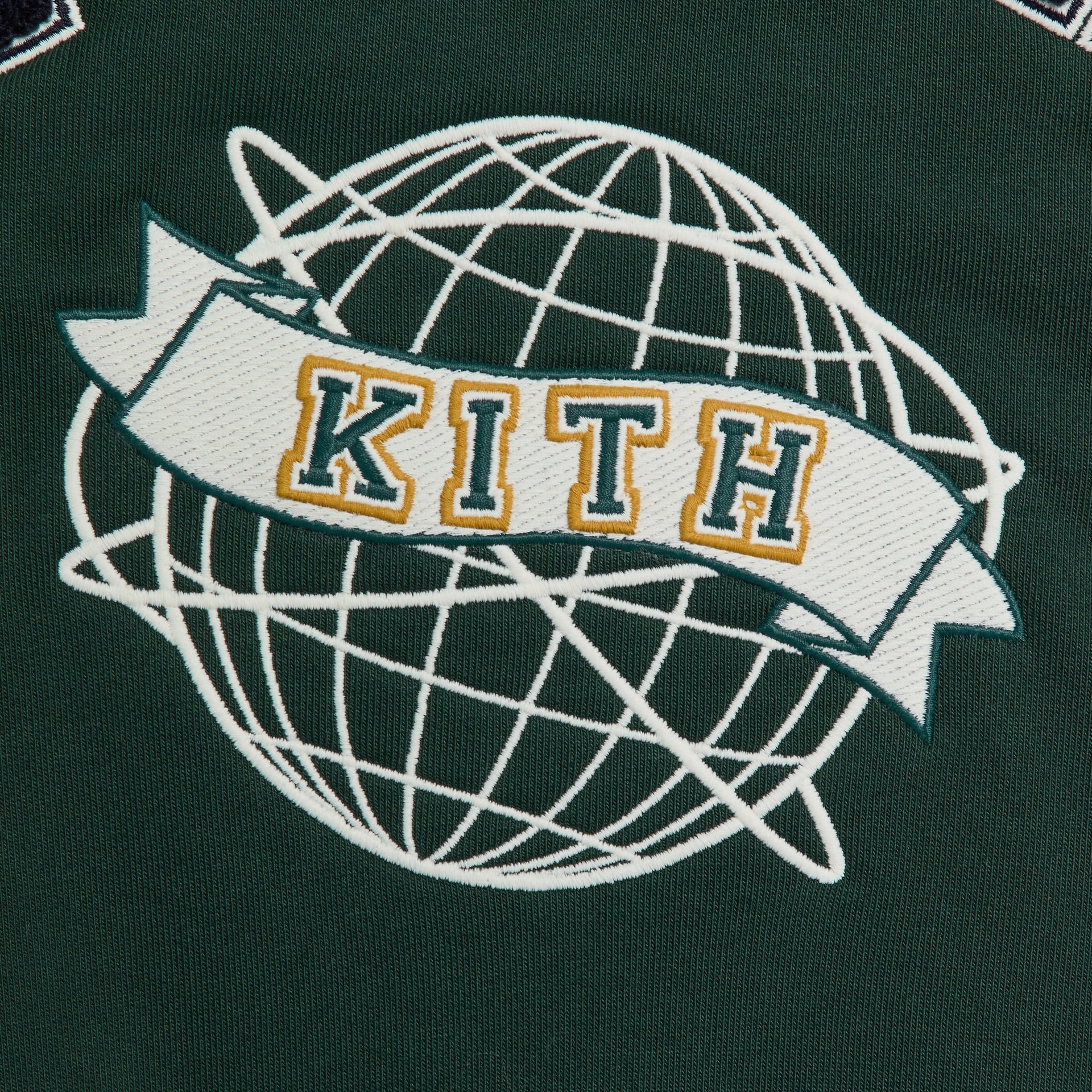 Close-up of the Kith Baby Varsity Jacket's embroidered globe and Kith banner patch on green wool in Stadium colorway