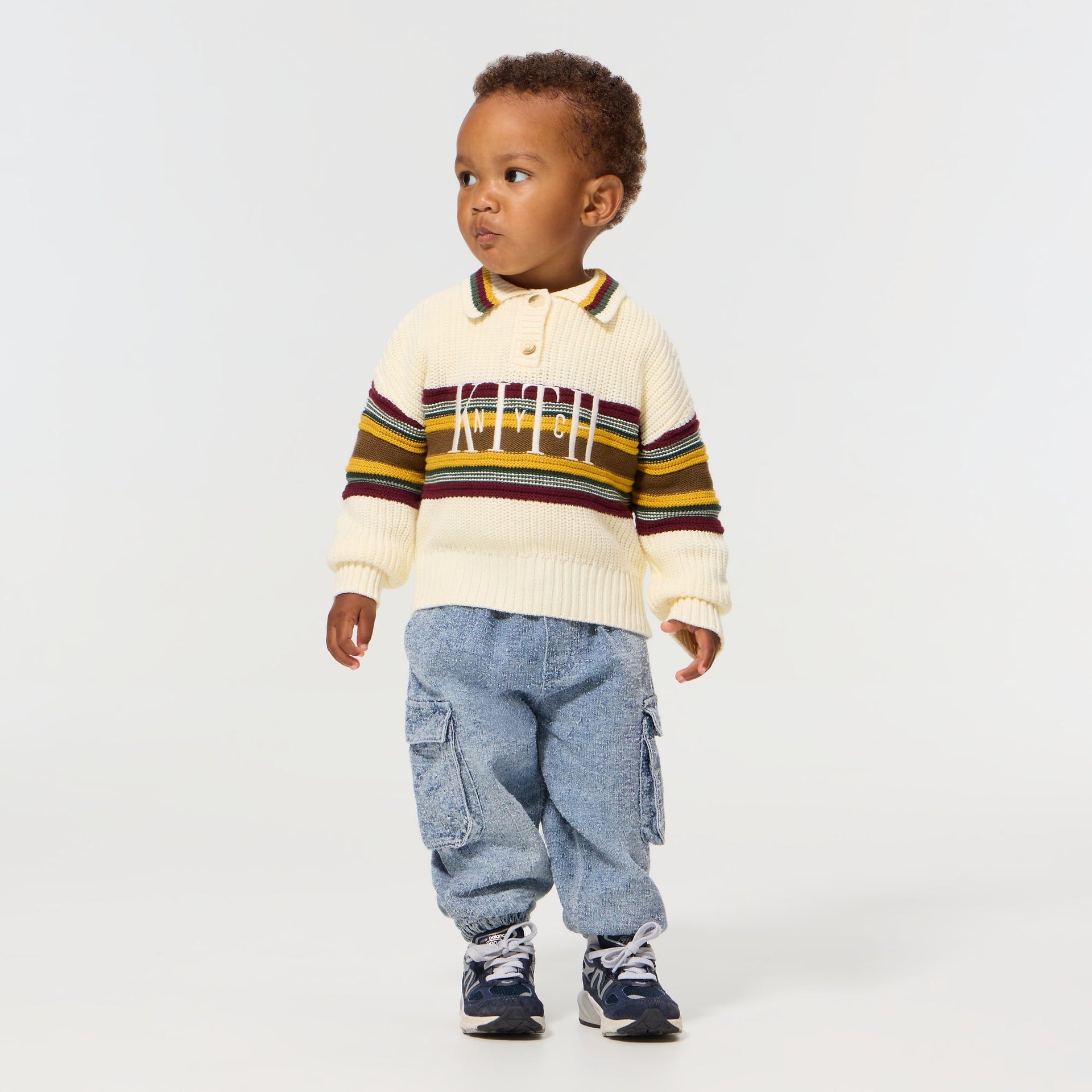 Baby wearing the Kith Baby Chunky Knit Rugby Shirt in Sandrift with denim cargo pants and sneakers