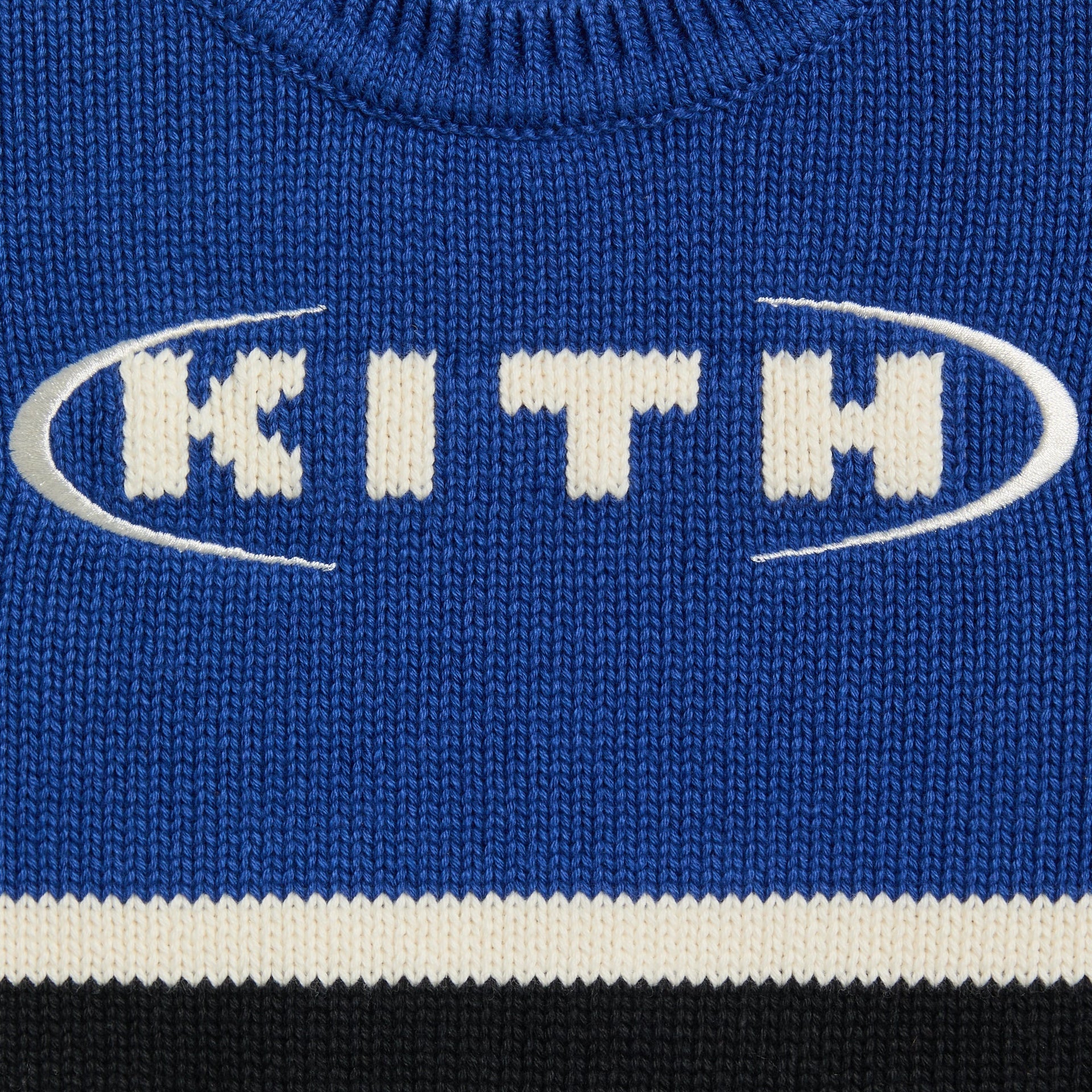 Close-up of the Kith Baby Varsity Nelson Knit Crewneck's embroidered Kith oval logo on blue knit
