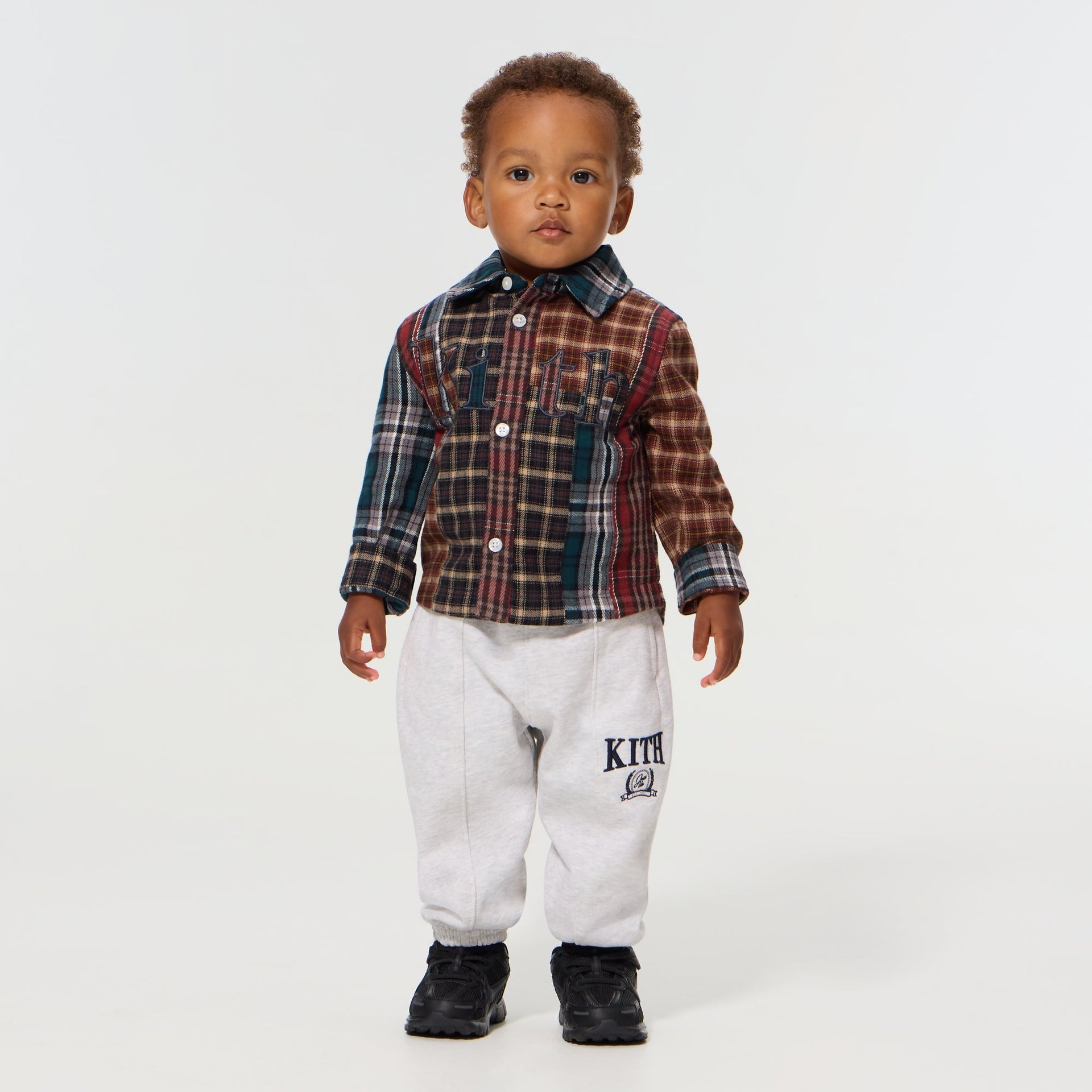 Baby wearing the Kith Baby Patchwork Plaid Apollo Shirt in Chest with grey Kith sweatpants and black sneakers, front view