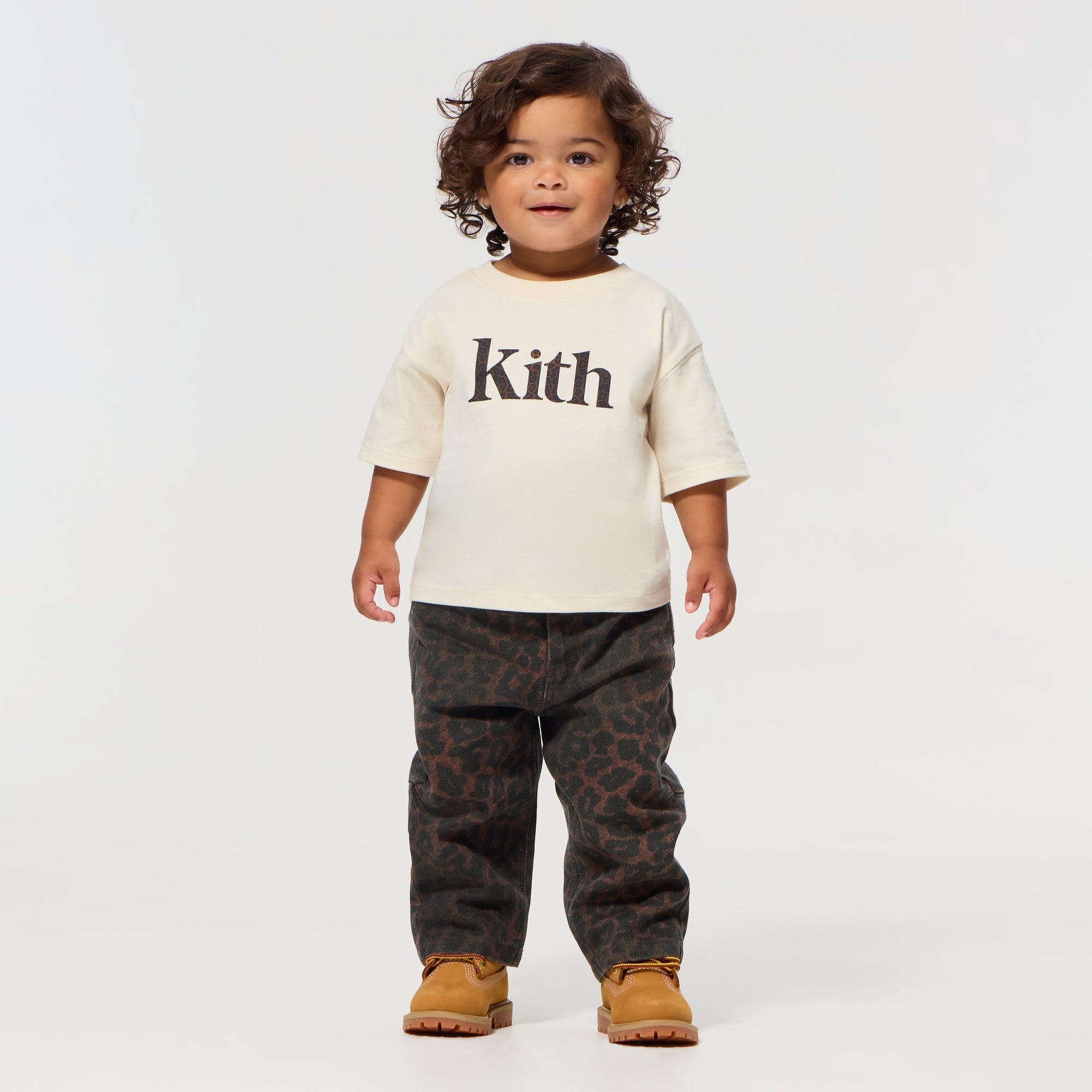 Toddler wearing the Kith Baby Leopard Kith Serif Leonard Tee in Sandrift with leopard-print pants and tan boots