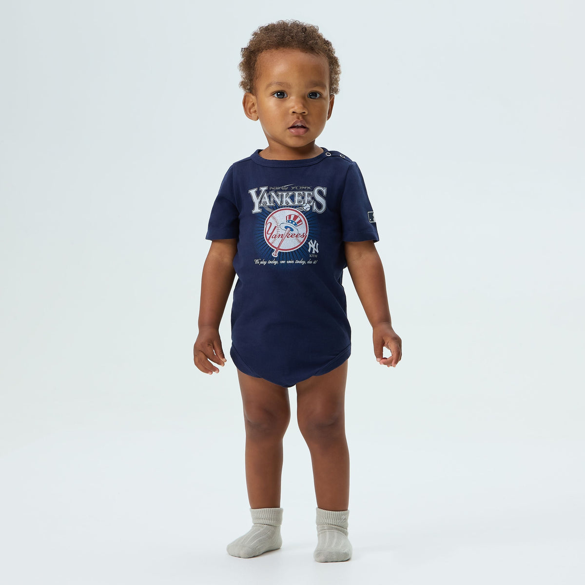 Kith Baby for the New York Yankees Legacy Bodysuit in Nocturnal navy, worn by a baby model, close-up front view