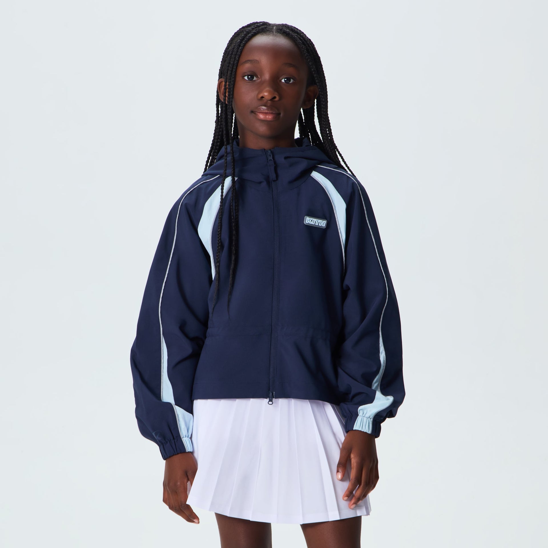 Kith Kids Lora Windbreaker Jacket in navy worn by young girl on-model with white pleated skirt, front view