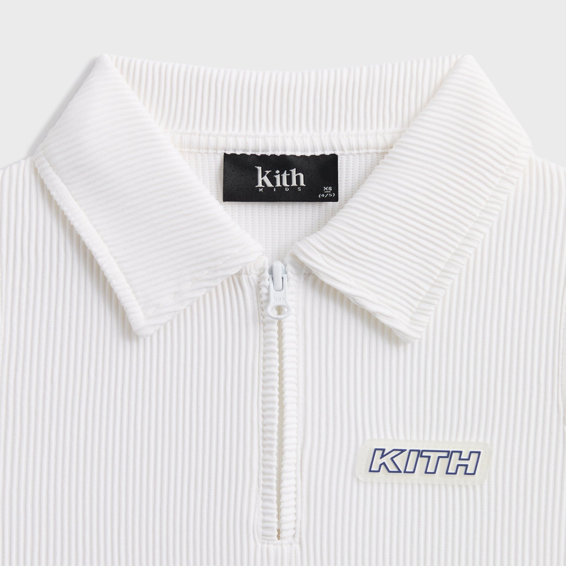 Kith Kids Active Fairway Polo in white, close-up of half-zip collar, Kith Kids label and KITH patch