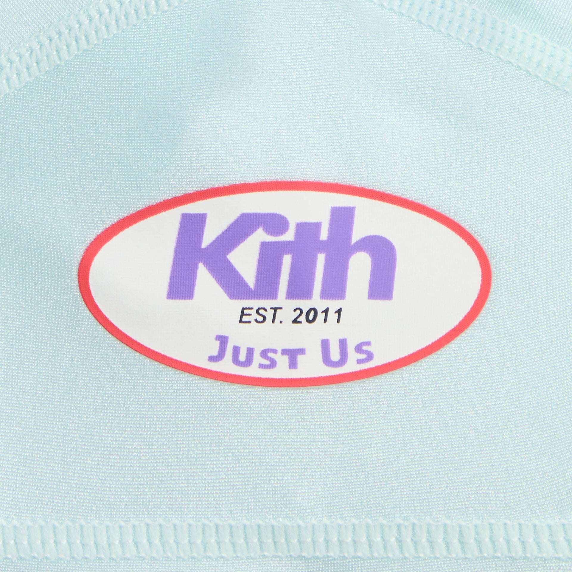 Kith Kids tee close-up of red oval Kith Just Us Est. 2011 sleeve patch on light blue fabric