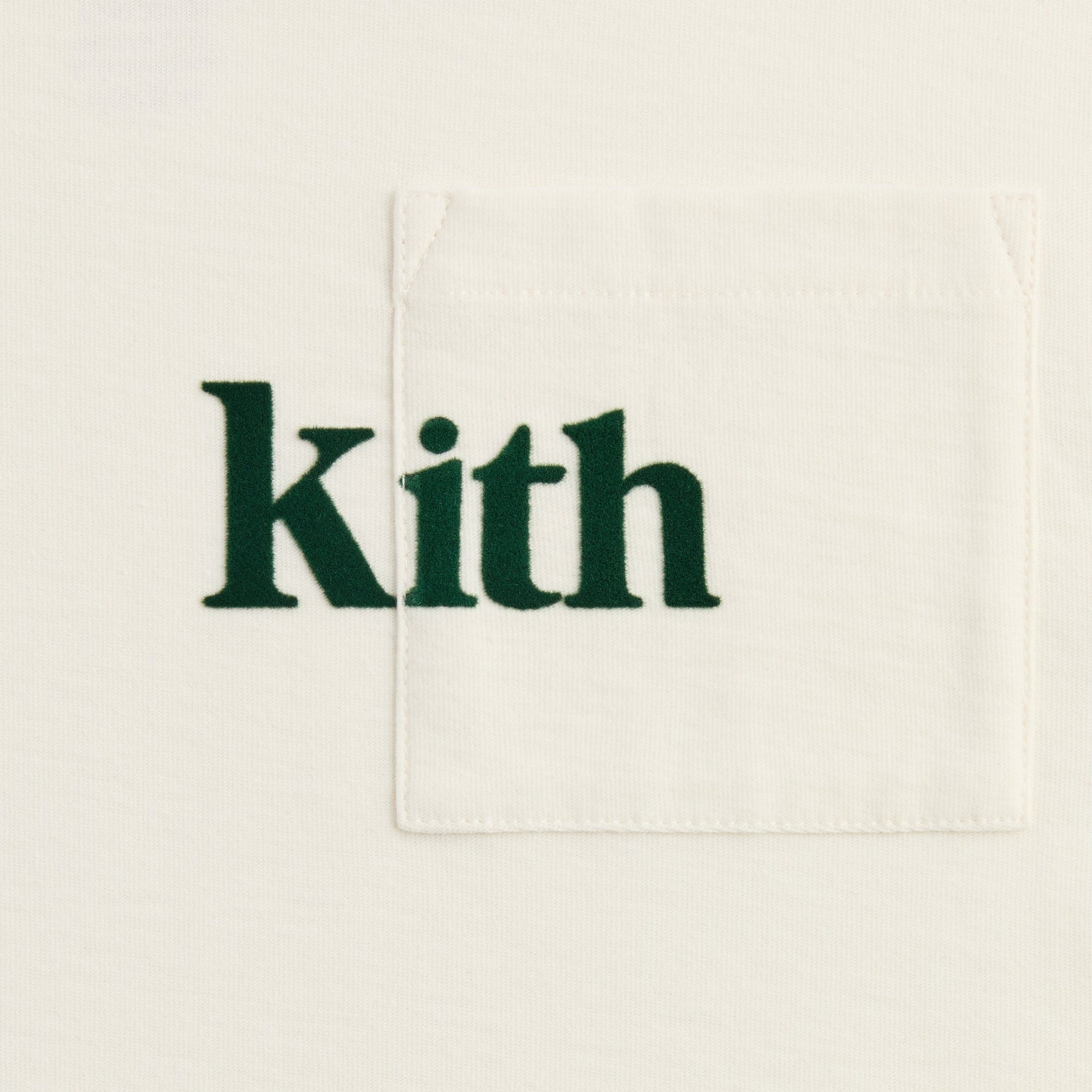 Close-up of the chest pocket with green Kith logo on the cream Kith Kids Quinn tee