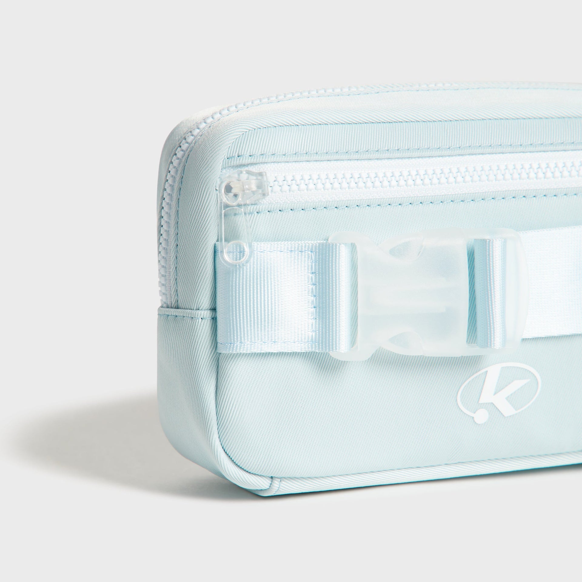 Detail of the clear buckle and webbing strap on the light blue Kith Kids Active belt bag with K logo