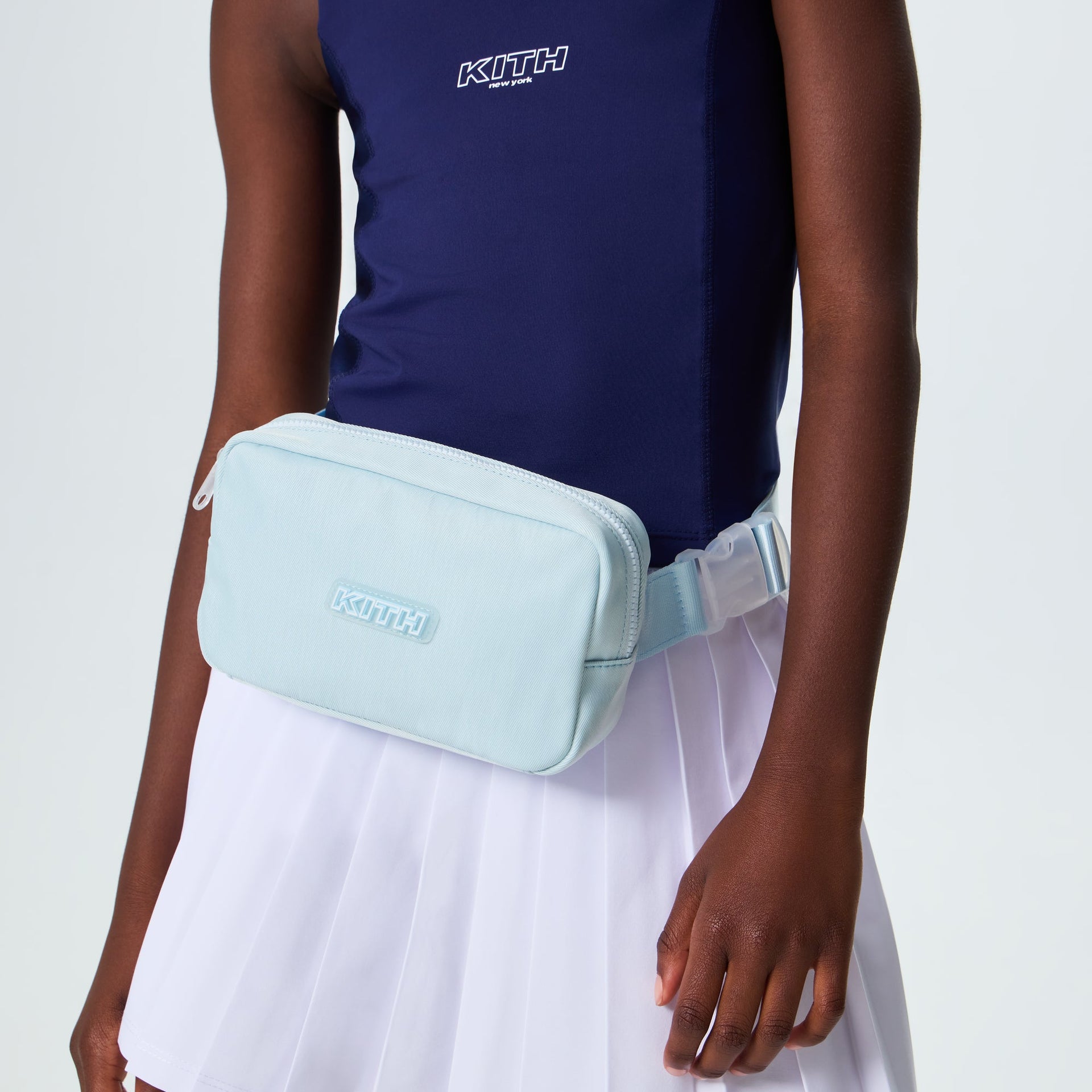 Kith Kids Active belt bag in light blue worn at the waist by a model in a navy top and white skirt