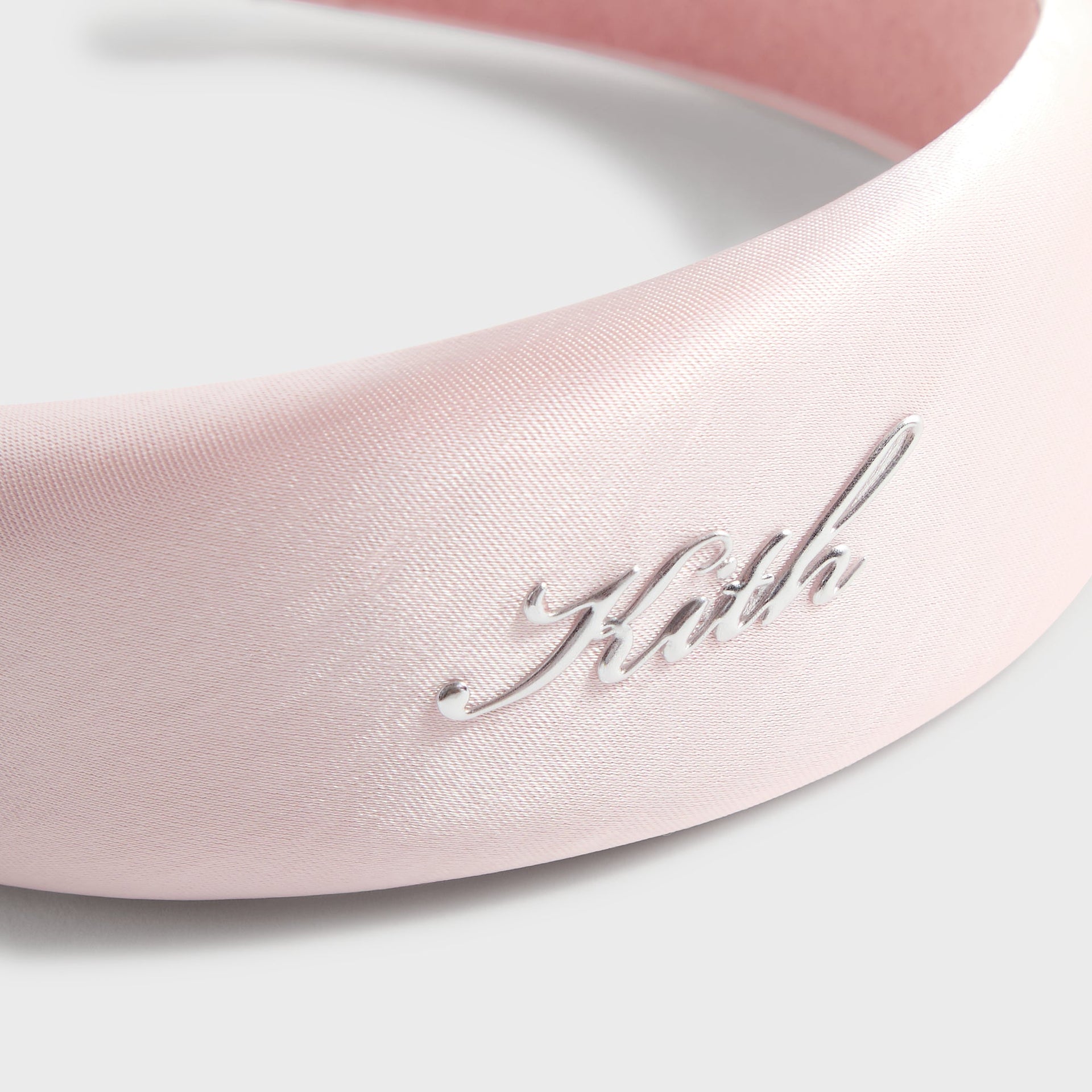 Kith Kids Satin Headband, close-up of silver metal Kith script logo on pink satin