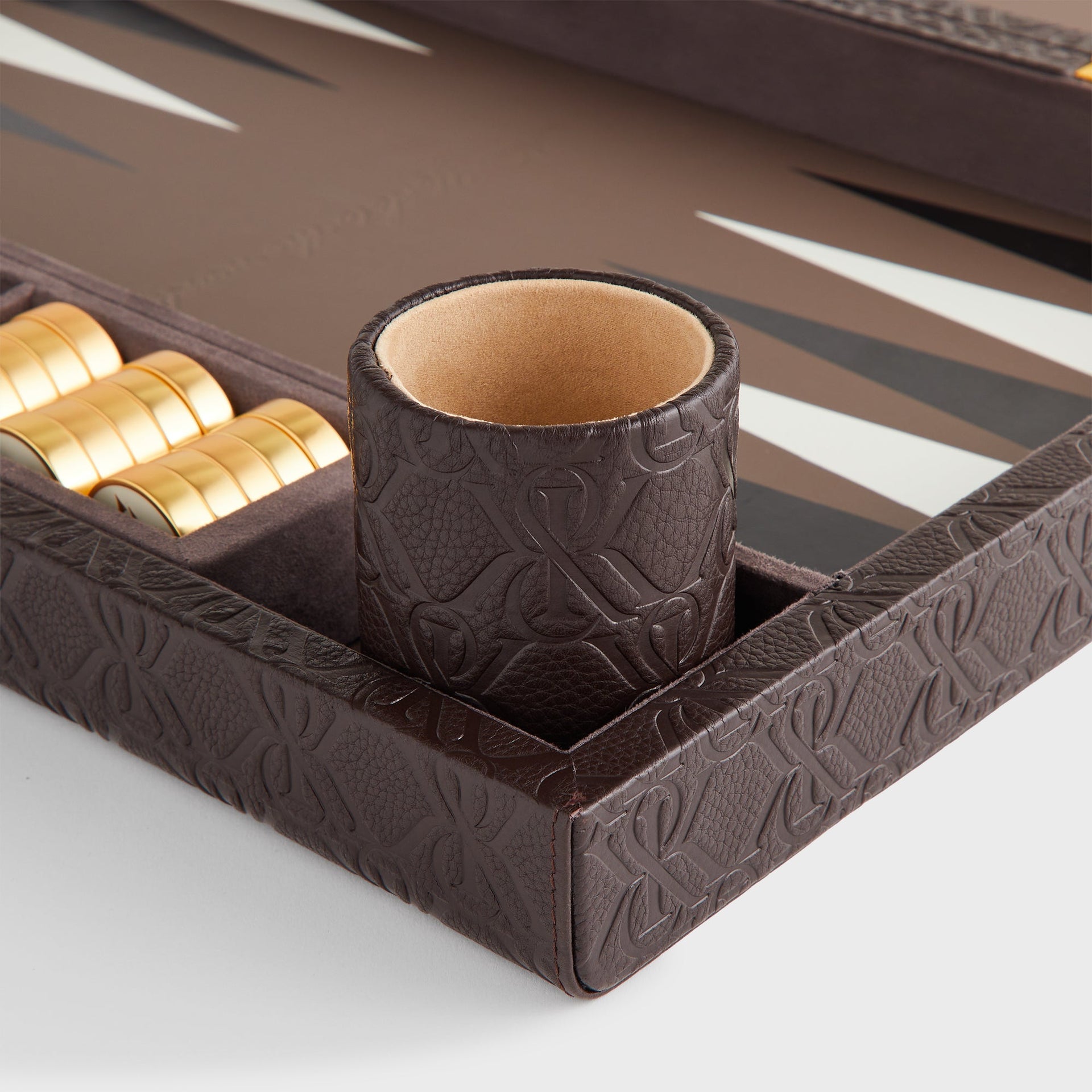Detail of the embossed leather dice cup with tan suede lining on the Kith Crest Monogram Backgammon Board
