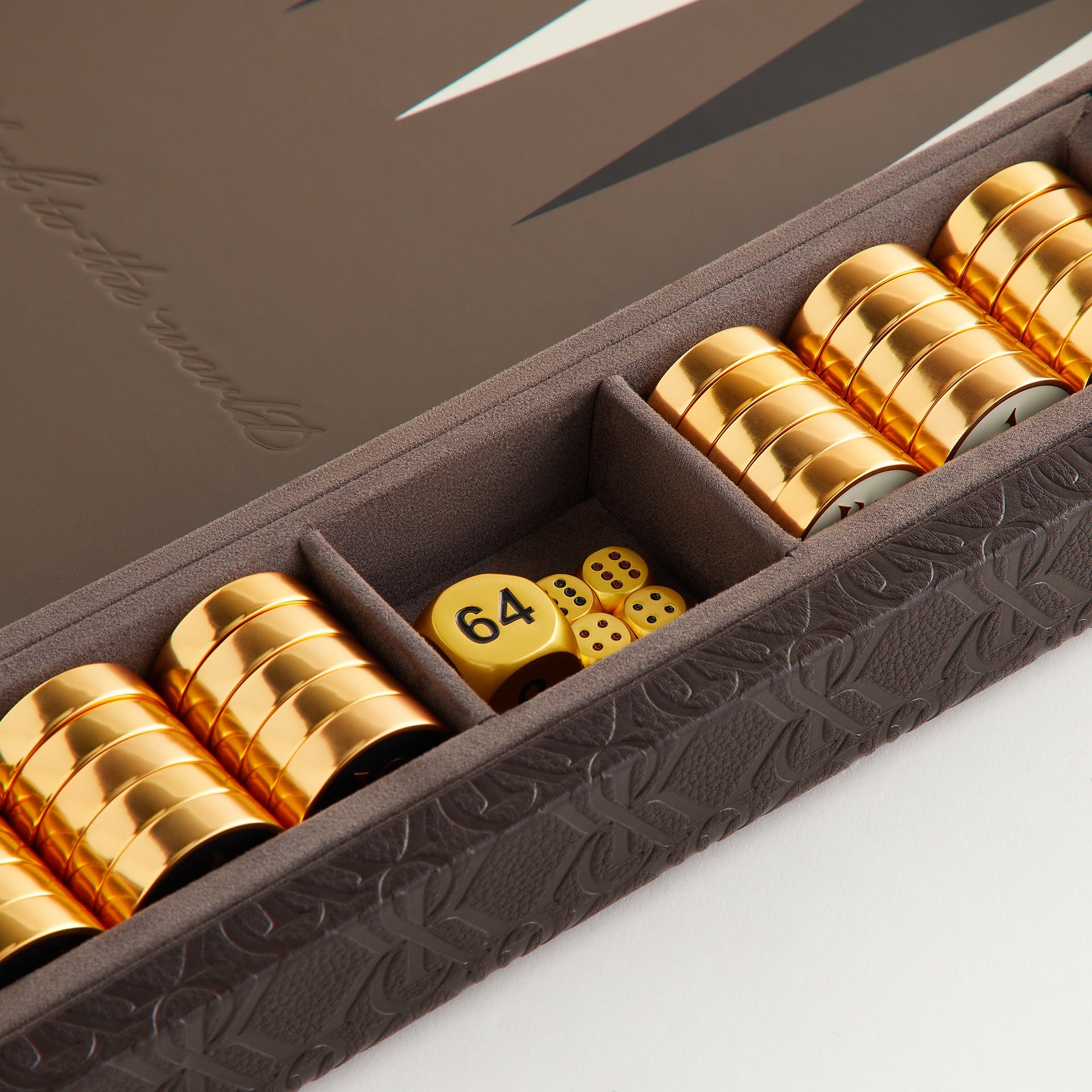 Angled close-up of gold checkers stacked beside the dice compartment on the Kith Crest Monogram Backgammon Board
