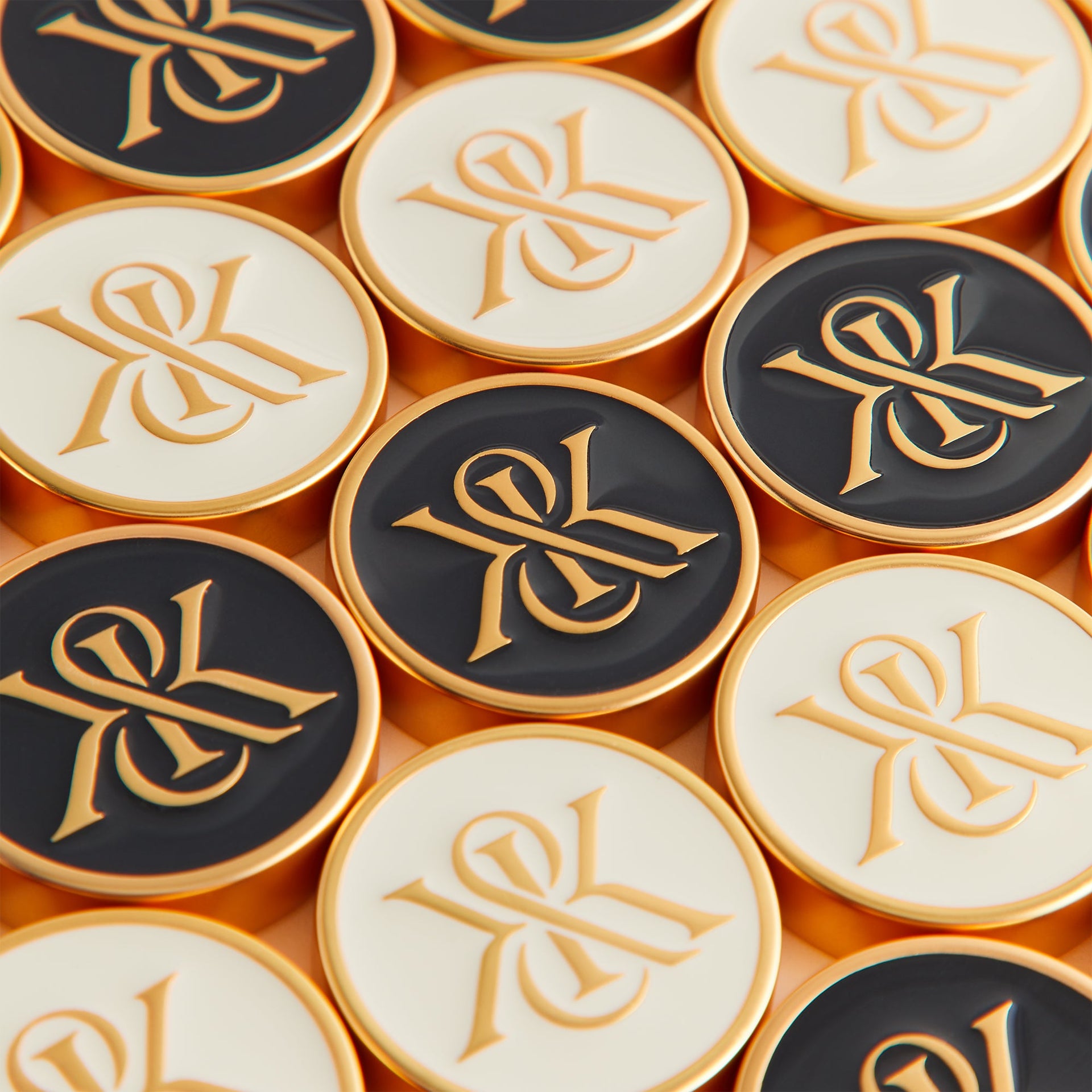 Close-up of black and cream enamel checkers engraved with the gold Kith & Kin crest monogram