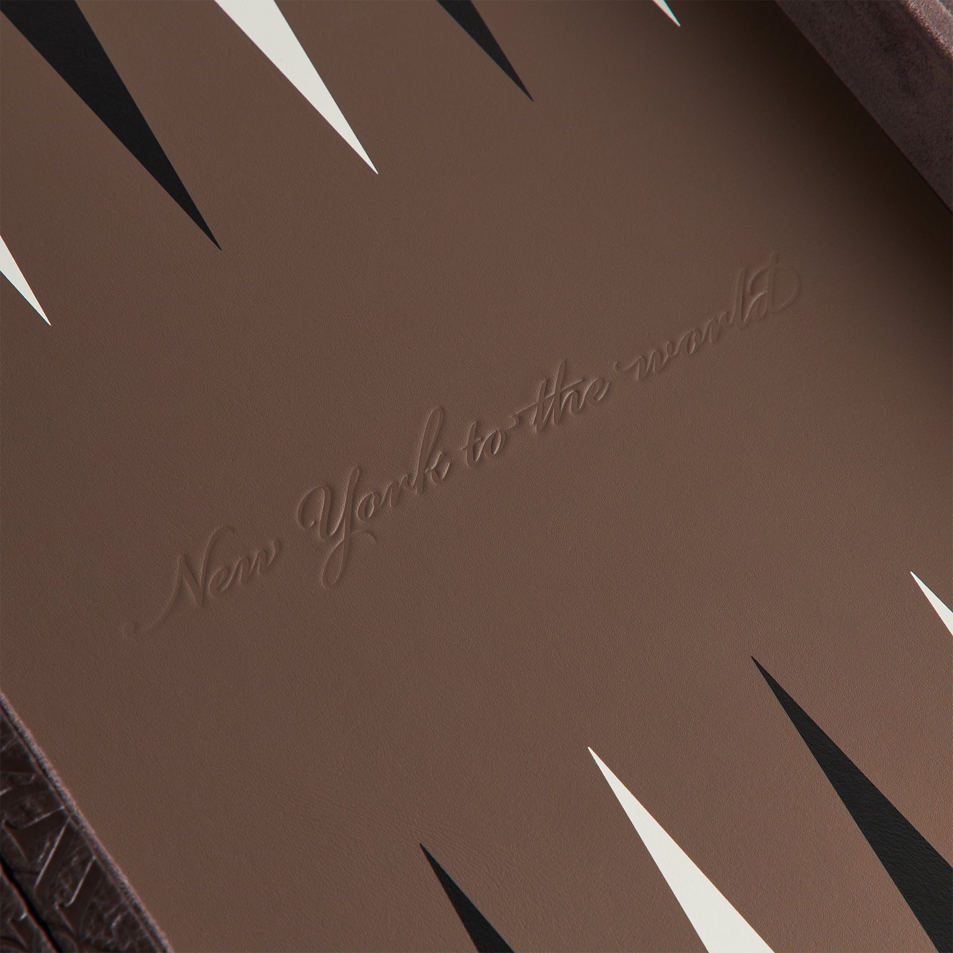 Close-up of the embossed New York to the World script detail on the Kith Crest Monogram Backgammon board surface