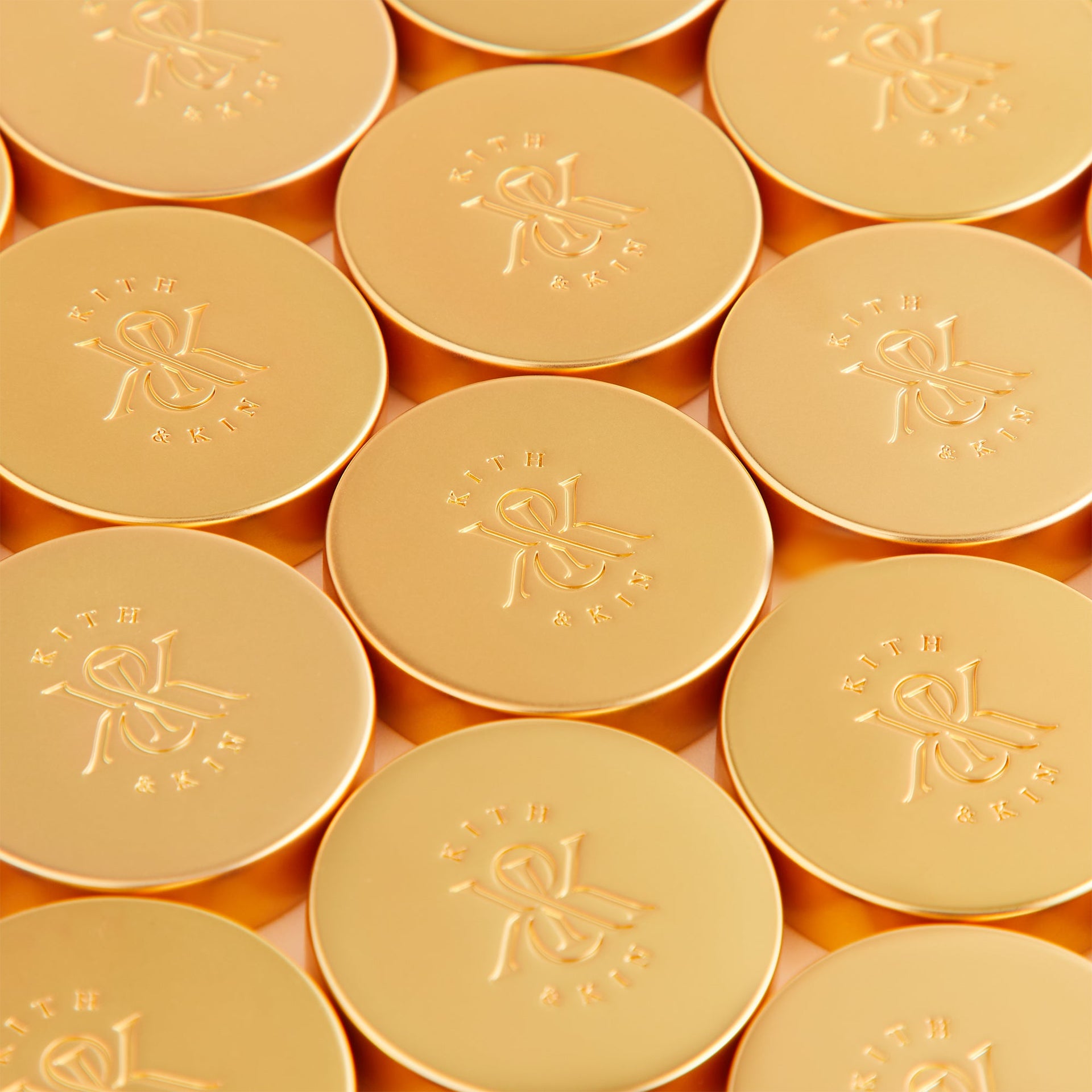 Macro detail of gold checker pieces stamped with the Kith & Kin New York crest logo