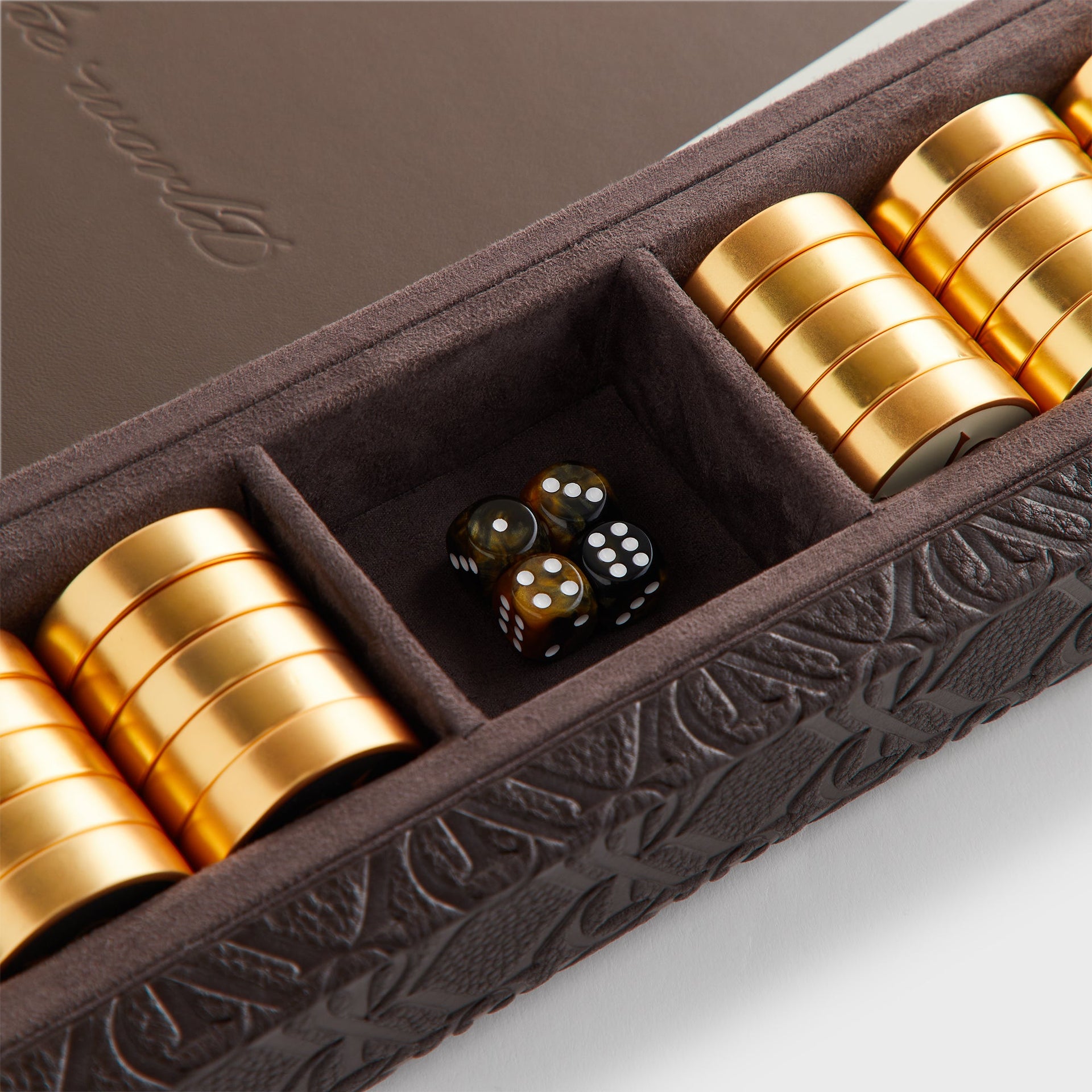 Close-up of gold checkers and tortoiseshell dice in the corner tray of the Kith Crest Monogram Backgammon Board
