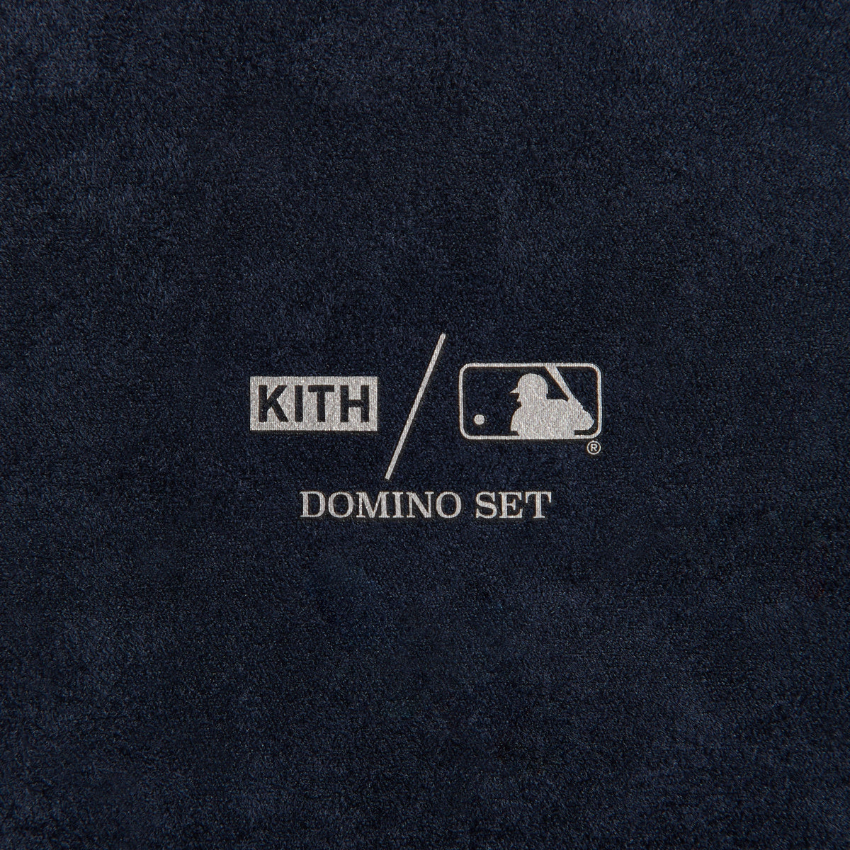 Close-up of the embossed cream NY logo patch on the domino case's navy leather exterior