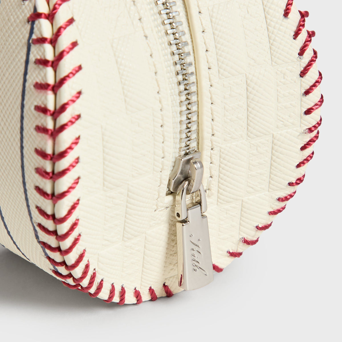 Close-up of the zipper pull engraved with the Kith script logo on the Sandrift baseball pouch