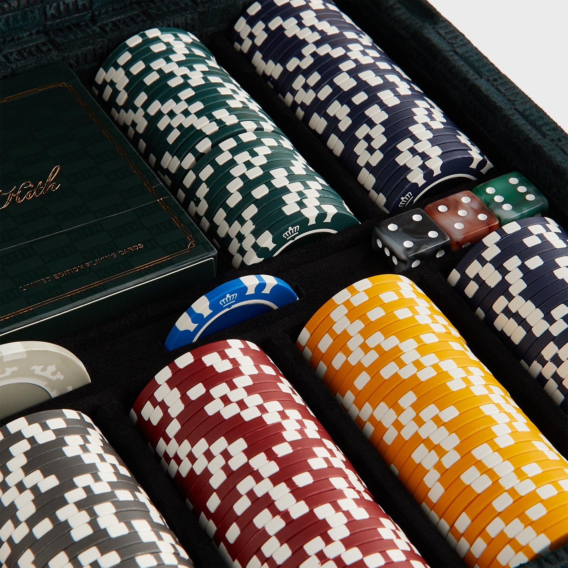 Angled close-up of green and navy Kith poker chip stacks with crown motif beside a Kith card deck and marbled dice
