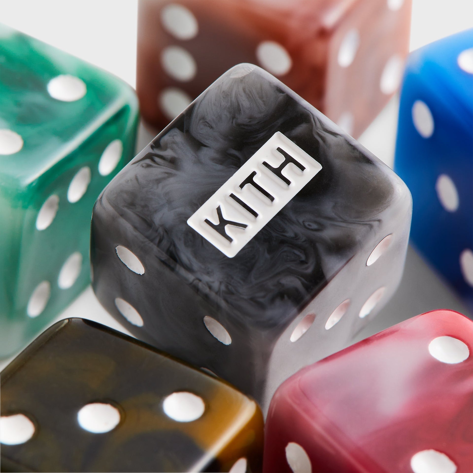 Macro of a black marbled Kith die embossed with the KITH logo among green, brown, blue and red swirled acrylic dice