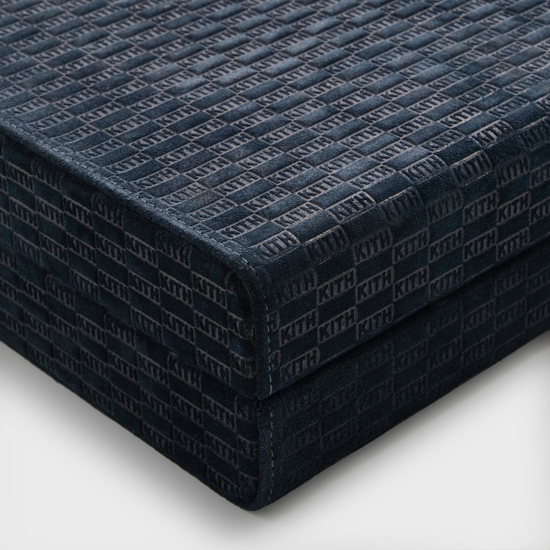 Corner of the closed Kith backgammon case in ink suede with allover embossed KITH monogram and stitched edges