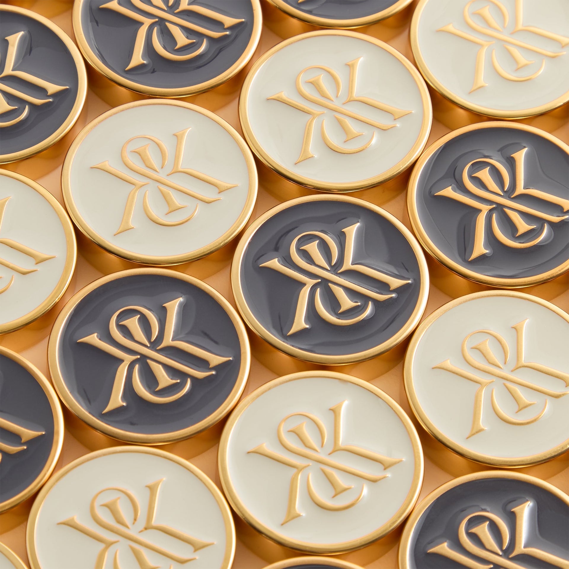 Grey and cream enamel backgammon checkers with gold Kith & Kin monogram and gold rims arranged in a tight grid