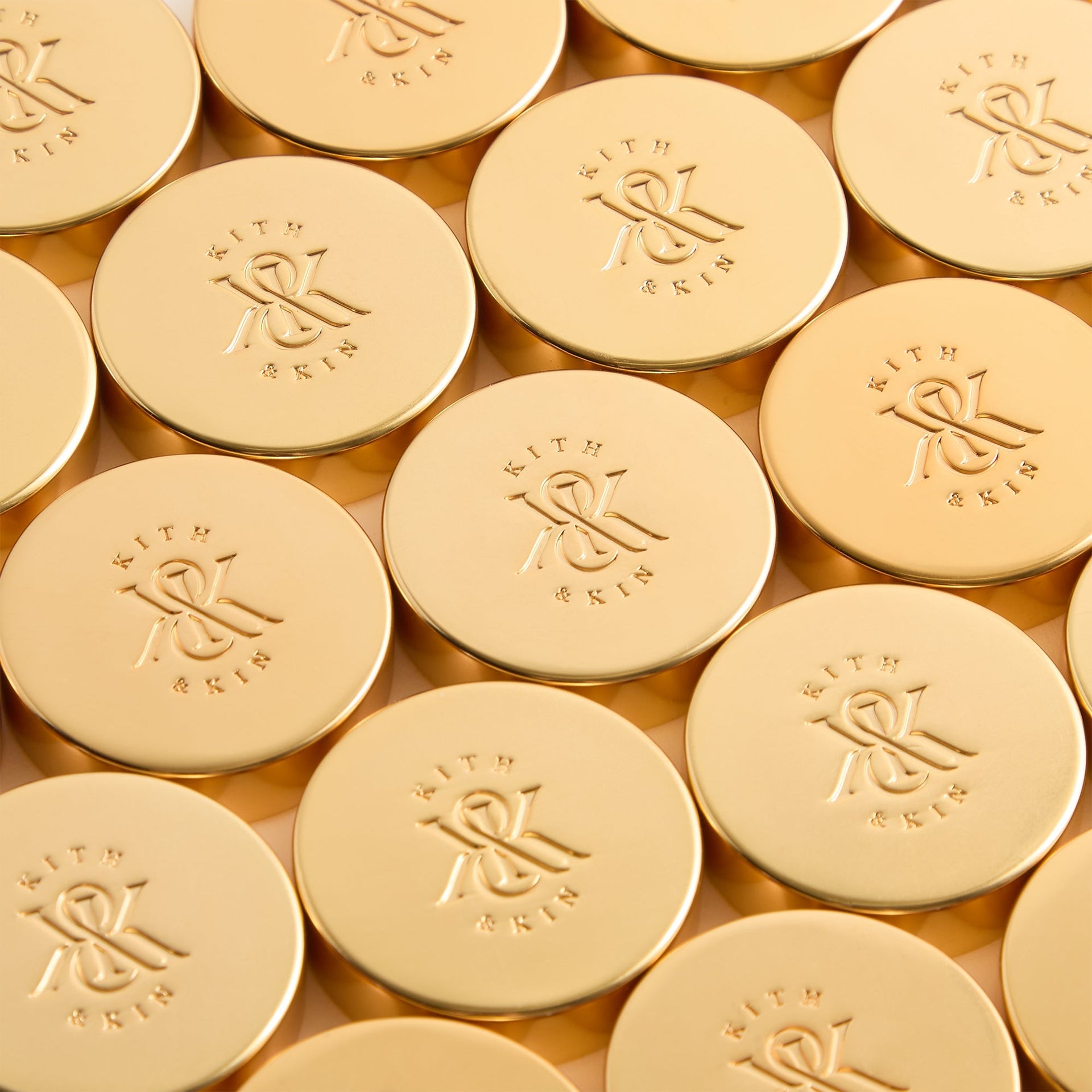 Reverse of the gold Kith backgammon checkers, each engraved with the Kith & Kin monogram, lined up in rows