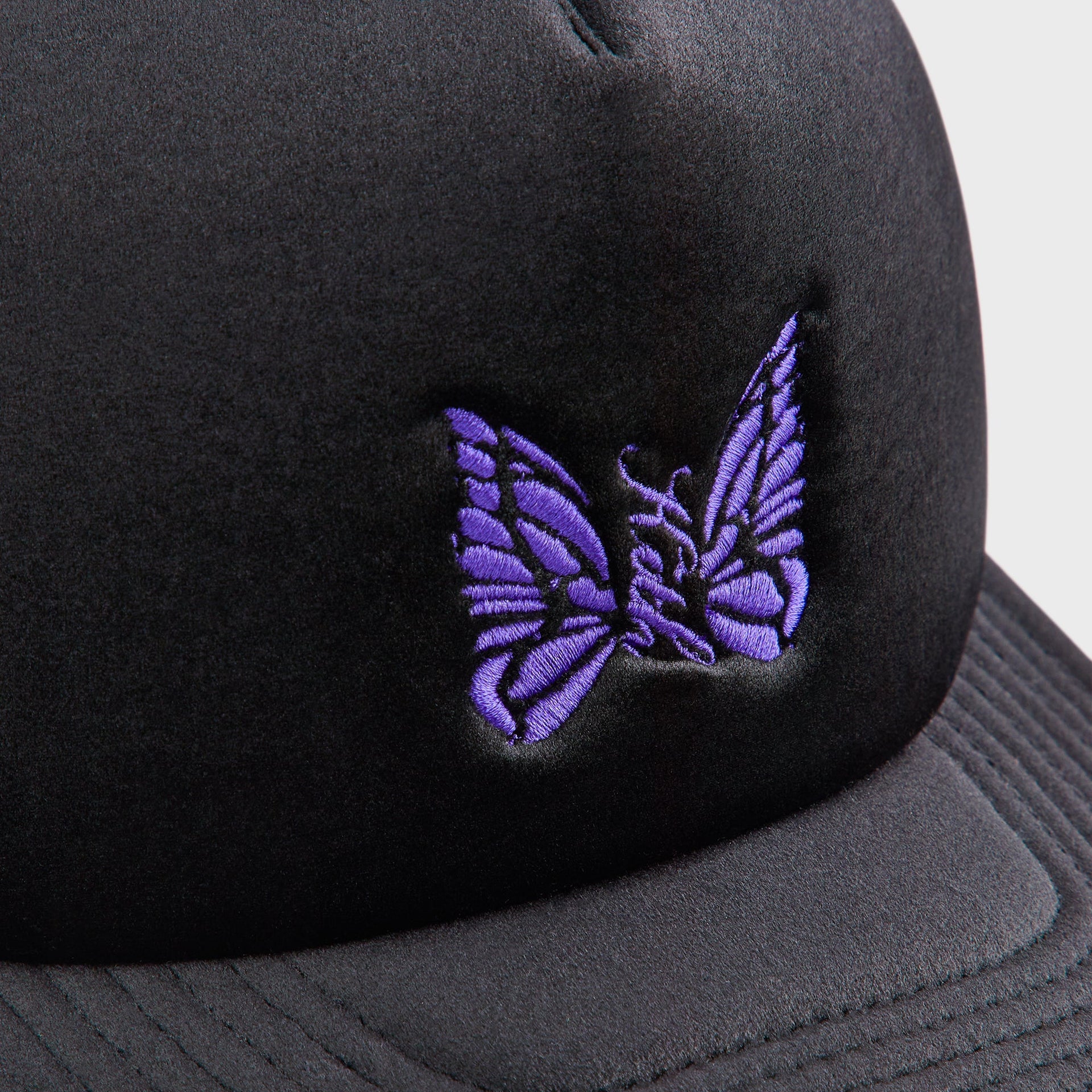 Close-up of the purple embroidered butterfly logo on the Kith for Needles Velour Nolan trucker cap