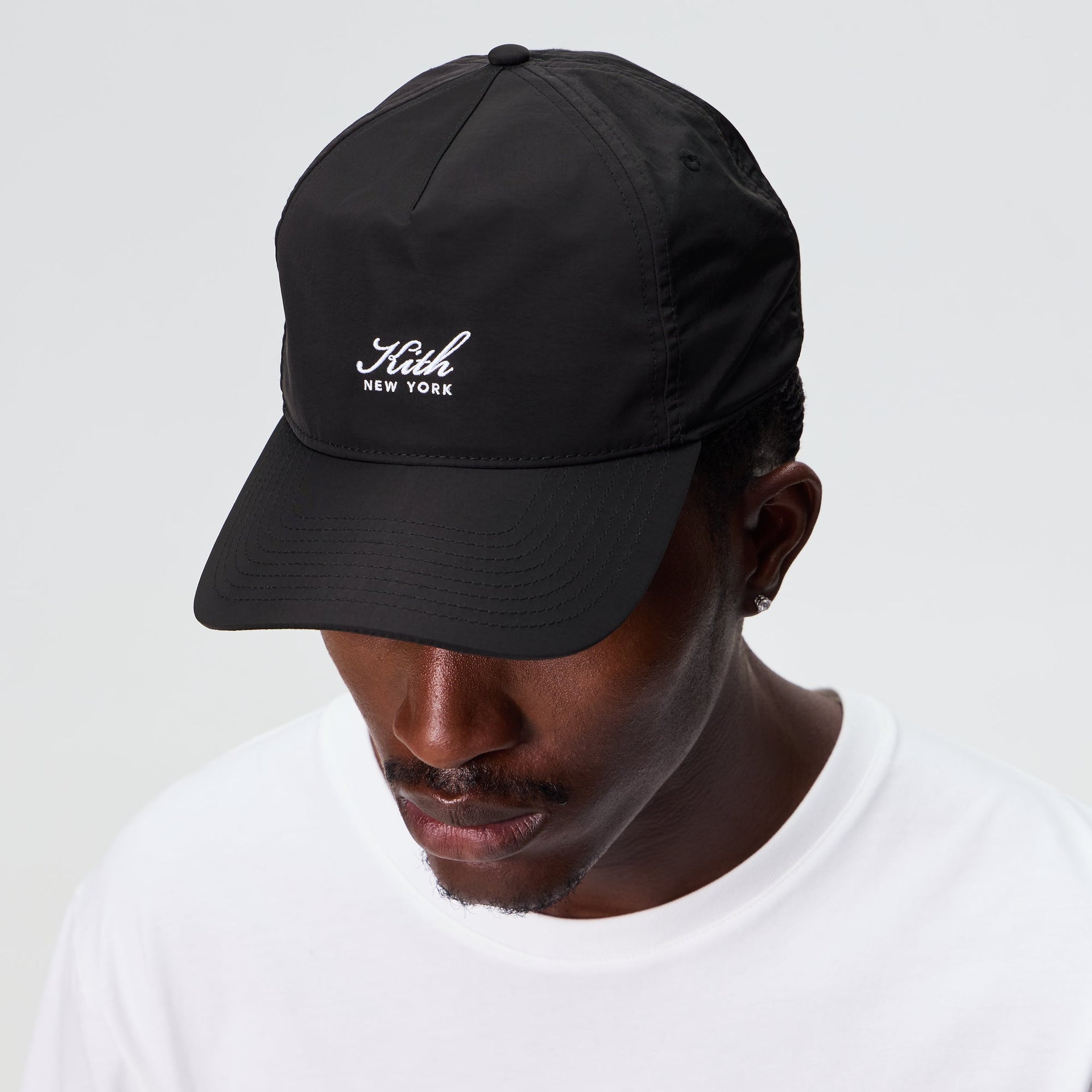 Man wearing the Kith Script Wrinkle Nylon Bay low pinch crown snapback in black