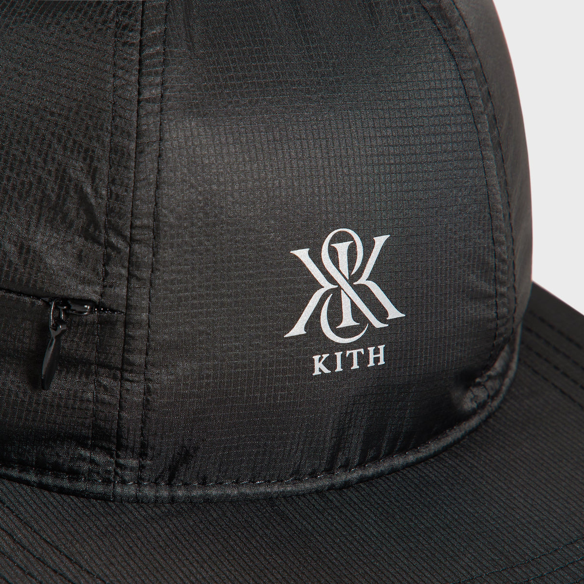 Close-up of the reflective Kith monogram logo and side zip pocket on the Marathon Cap