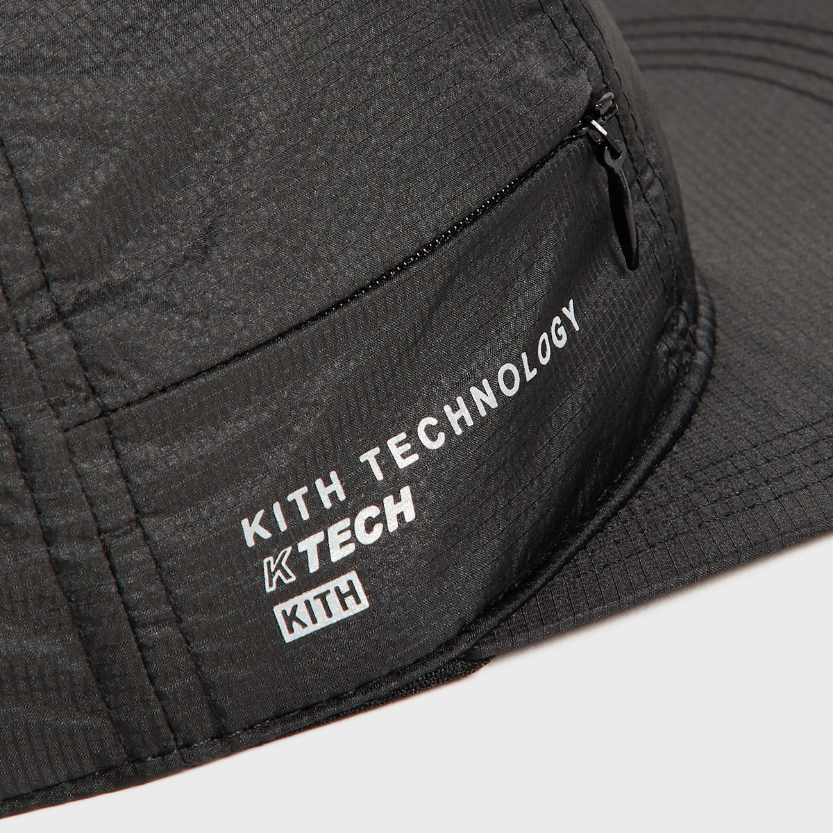 Close-up of the zip pocket and Kith Technology KTECH print near the brim of the Marathon Cap
