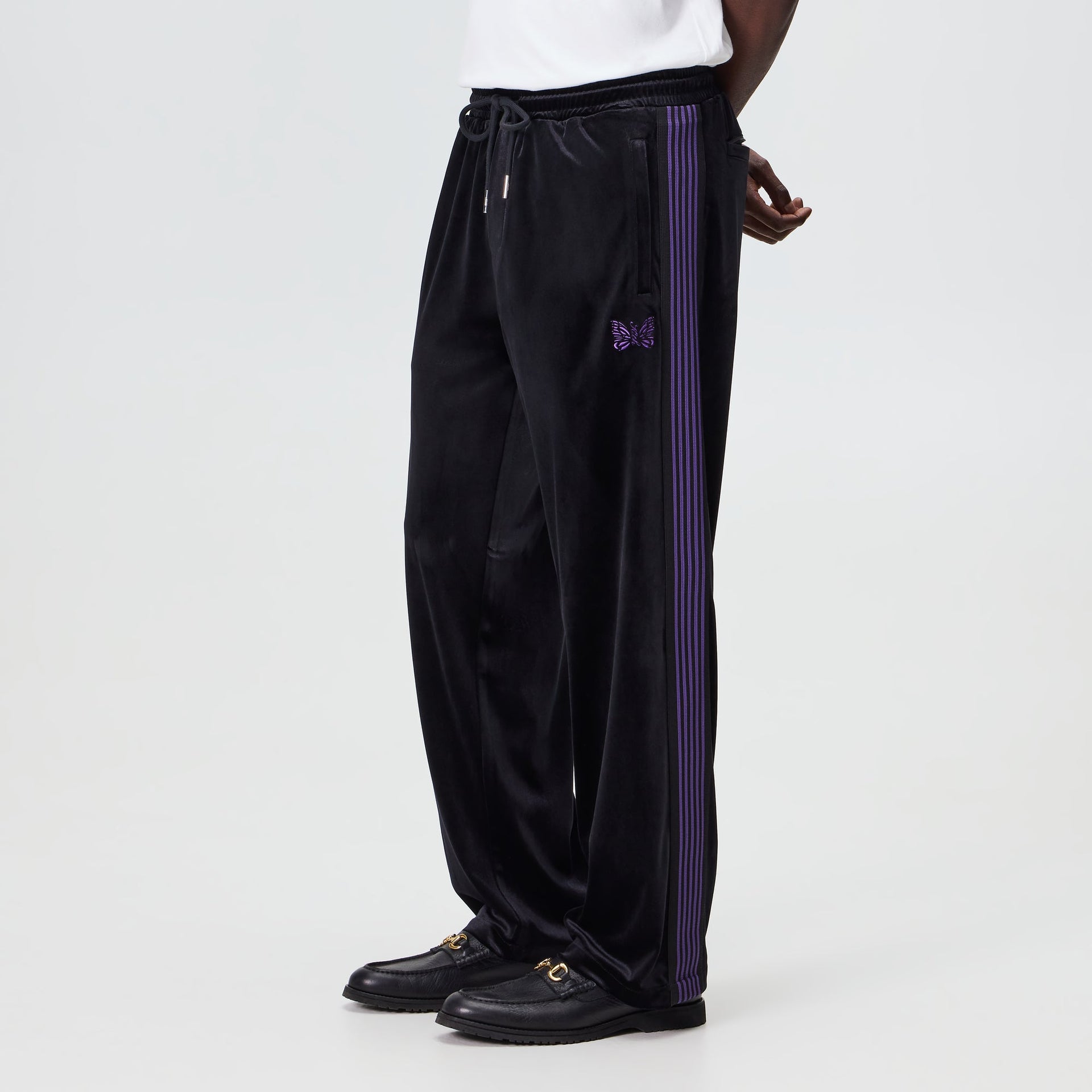 Man wearing the Kith for Needles Elias track pant in black velour with purple stripes