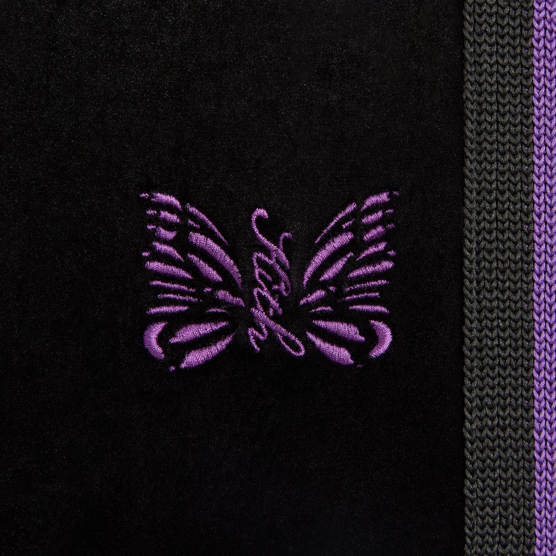 Close-up of the purple embroidered butterfly logo and striped side seam on the Elias track pant