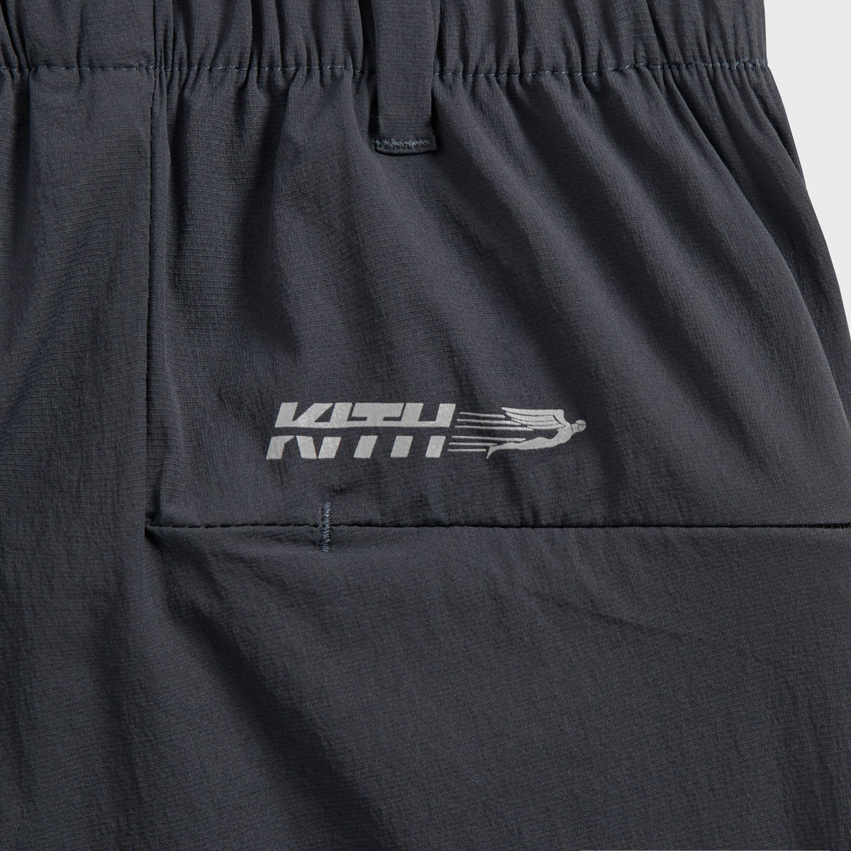 Close-up of Kith Four-Way Stretch Idris Pant back waistband with reflective Kith wordmark and wing logo