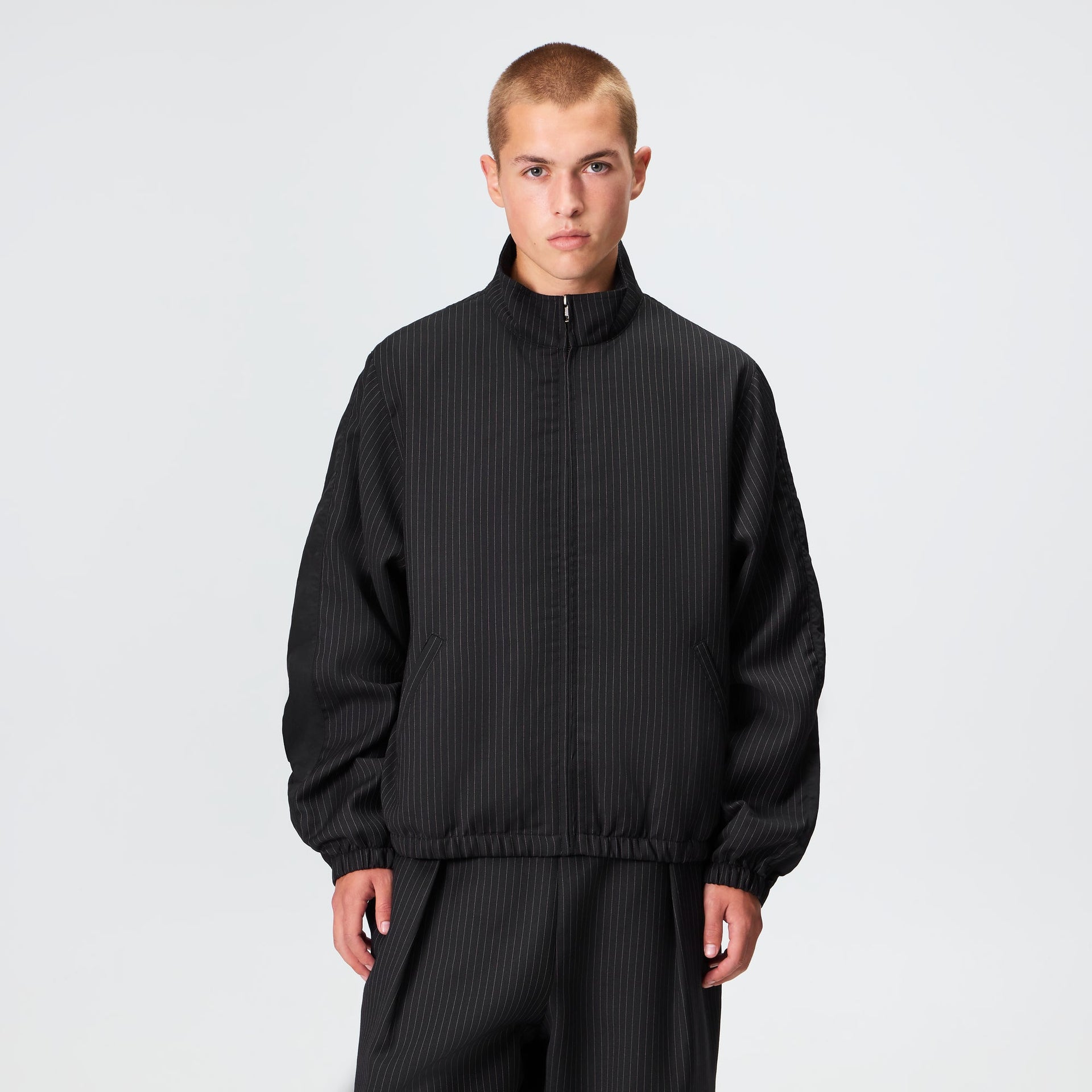Man wearing the Kith Pinstripe Rui track jacket in black with matching trousers