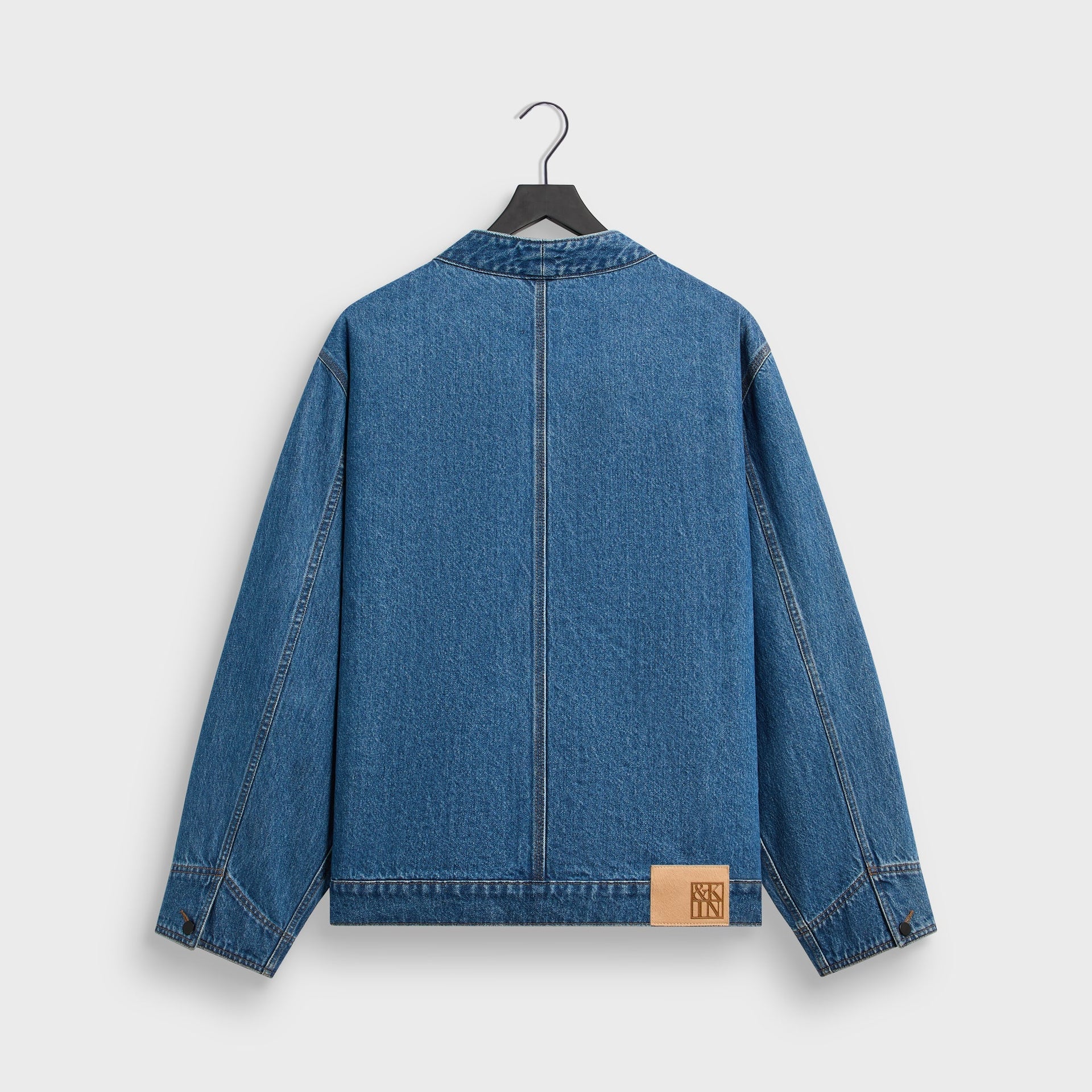 &Kin Clint Trucker Jacket, River Indigo denim, back view on hanger with center seam and tan leather logo patch at hem