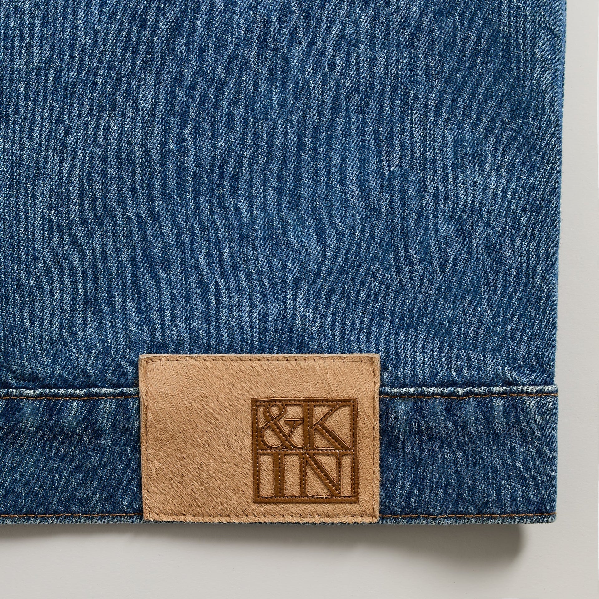 &Kin Clint Trucker Jacket detail, tan calf-hair &Kin logo patch stitched at the indigo denim hem