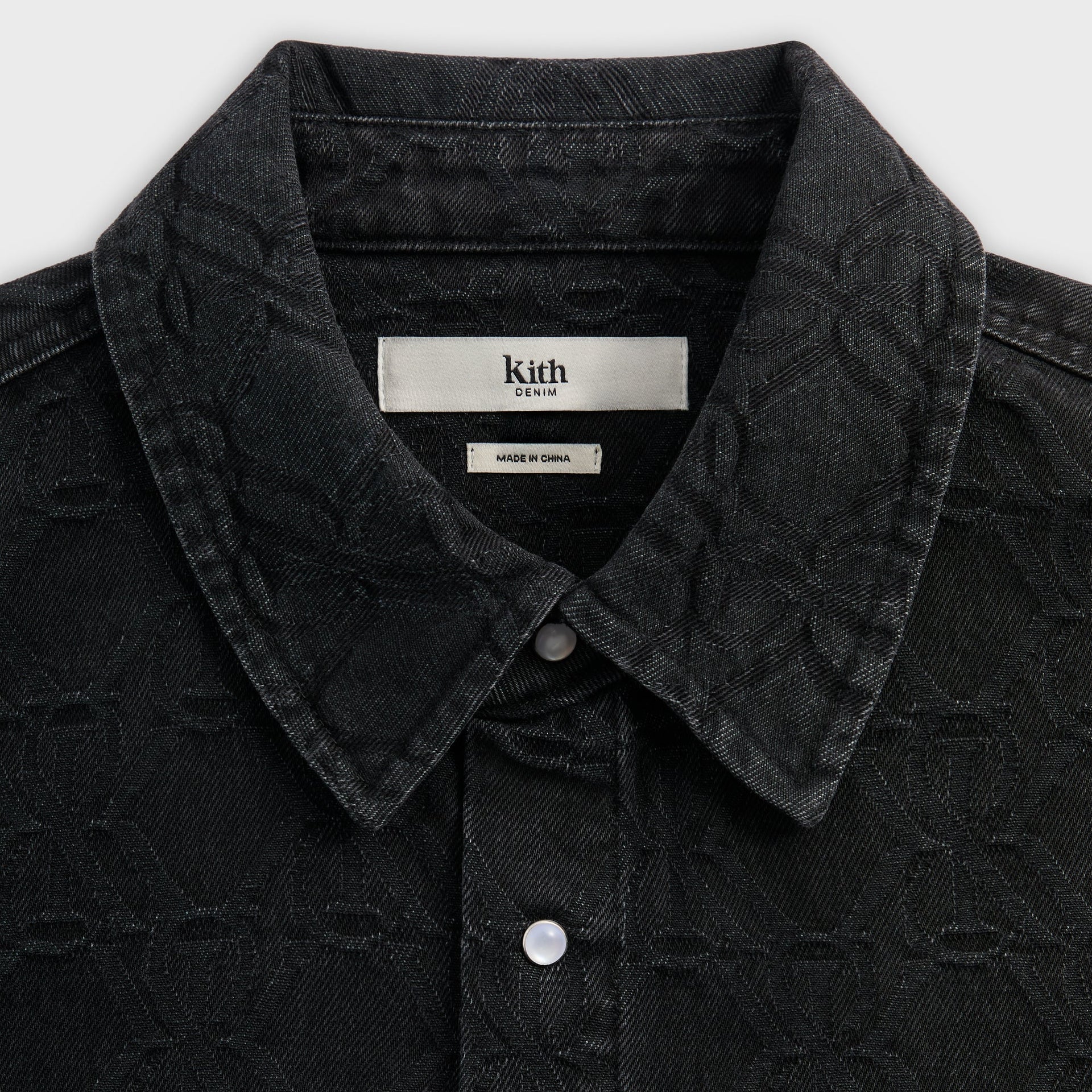 Close-up of the woven Kith collar label on the Jacquard Crest Apollo shirt in black denim