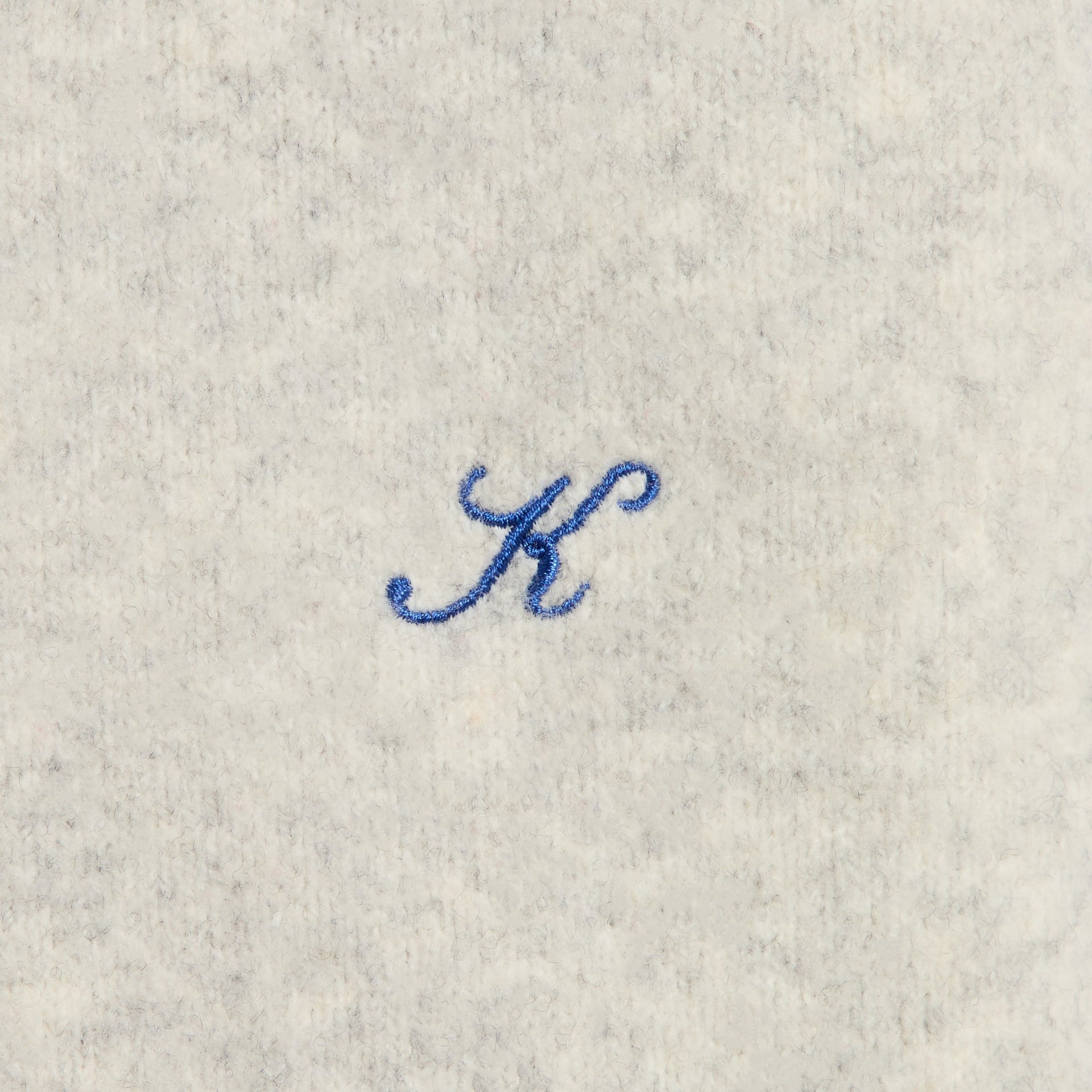Close-up of the blue embroidered K logo on the Kith Boucle Tobey polo in light heather grey