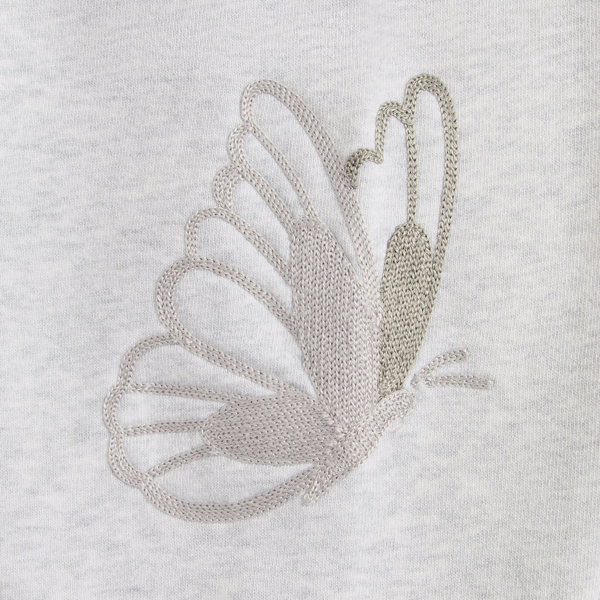 Close-up of the tonal embroidered butterfly graphic on the light heather grey Lawson crewneck sleeve