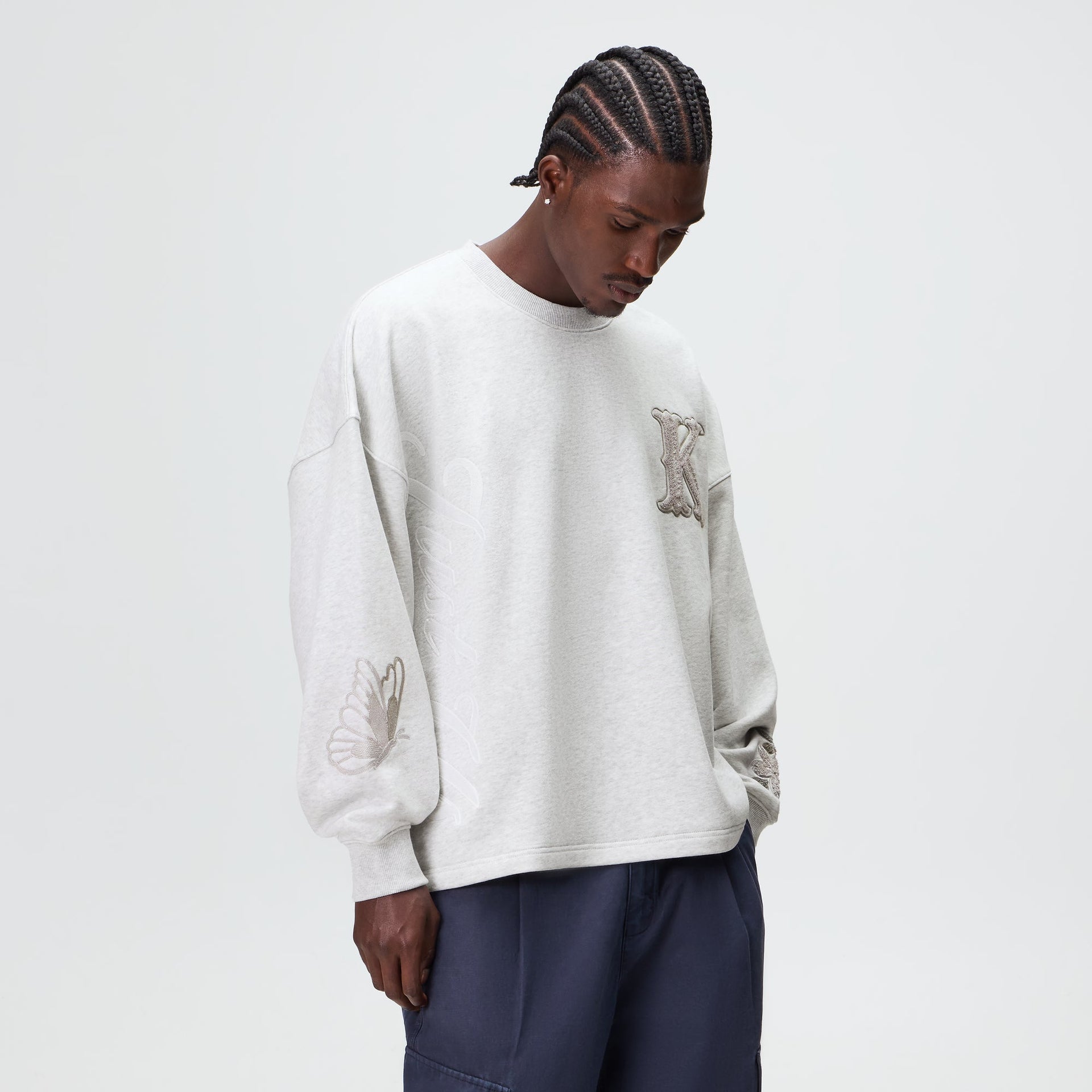 Man wearing the Kith Varsity Lawson crewneck in light heather grey with chenille K patch, front view
