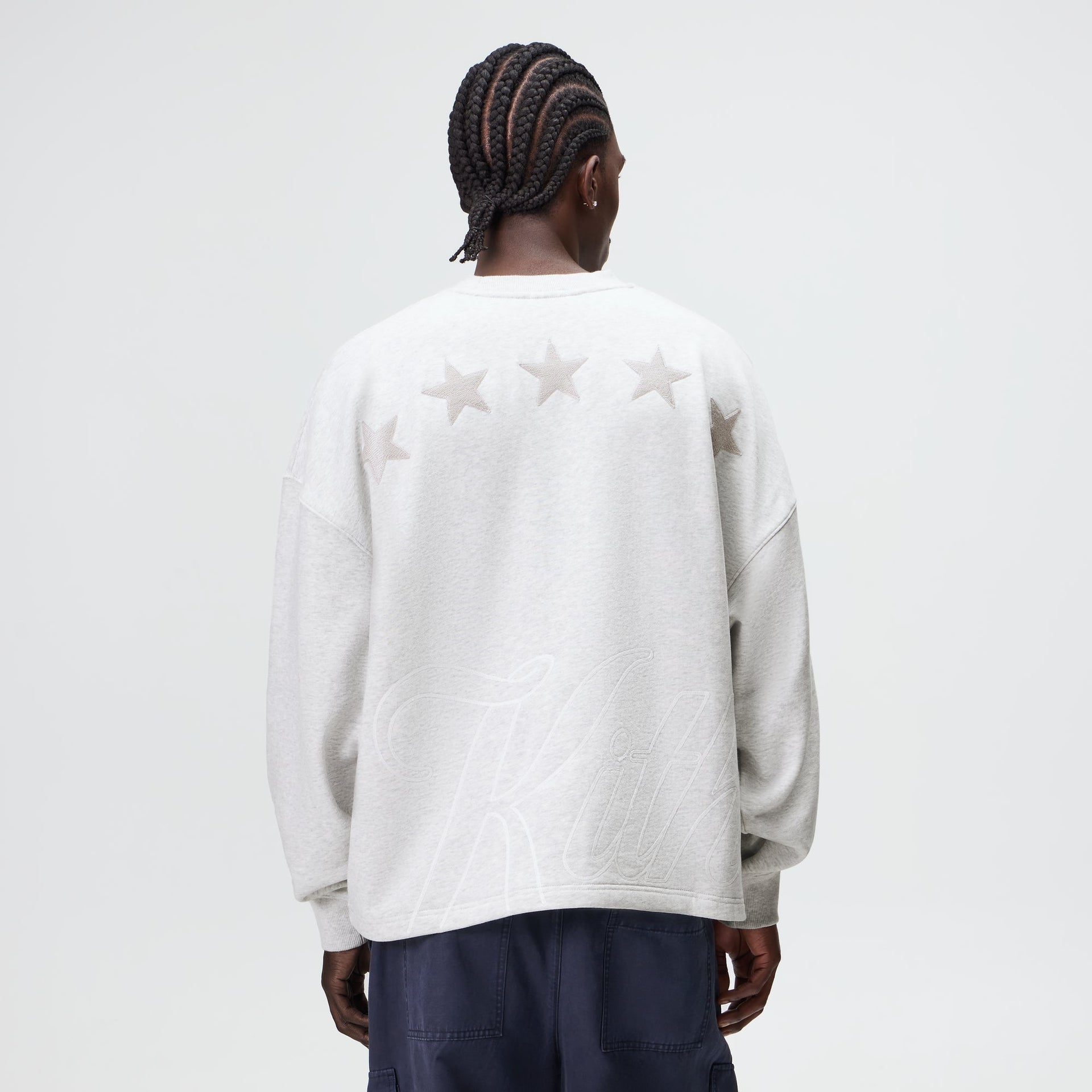 Man wearing the Kith Varsity Lawson crewneck in light heather grey, back view showing star and Kith script graphics