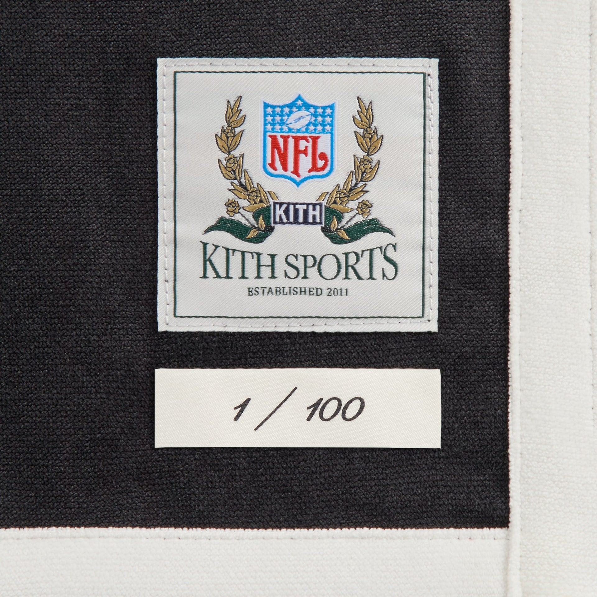 Close-up of the Kith Sports NFL woven label and 1 of 100 numbering tag on the Panthers Leon shirt