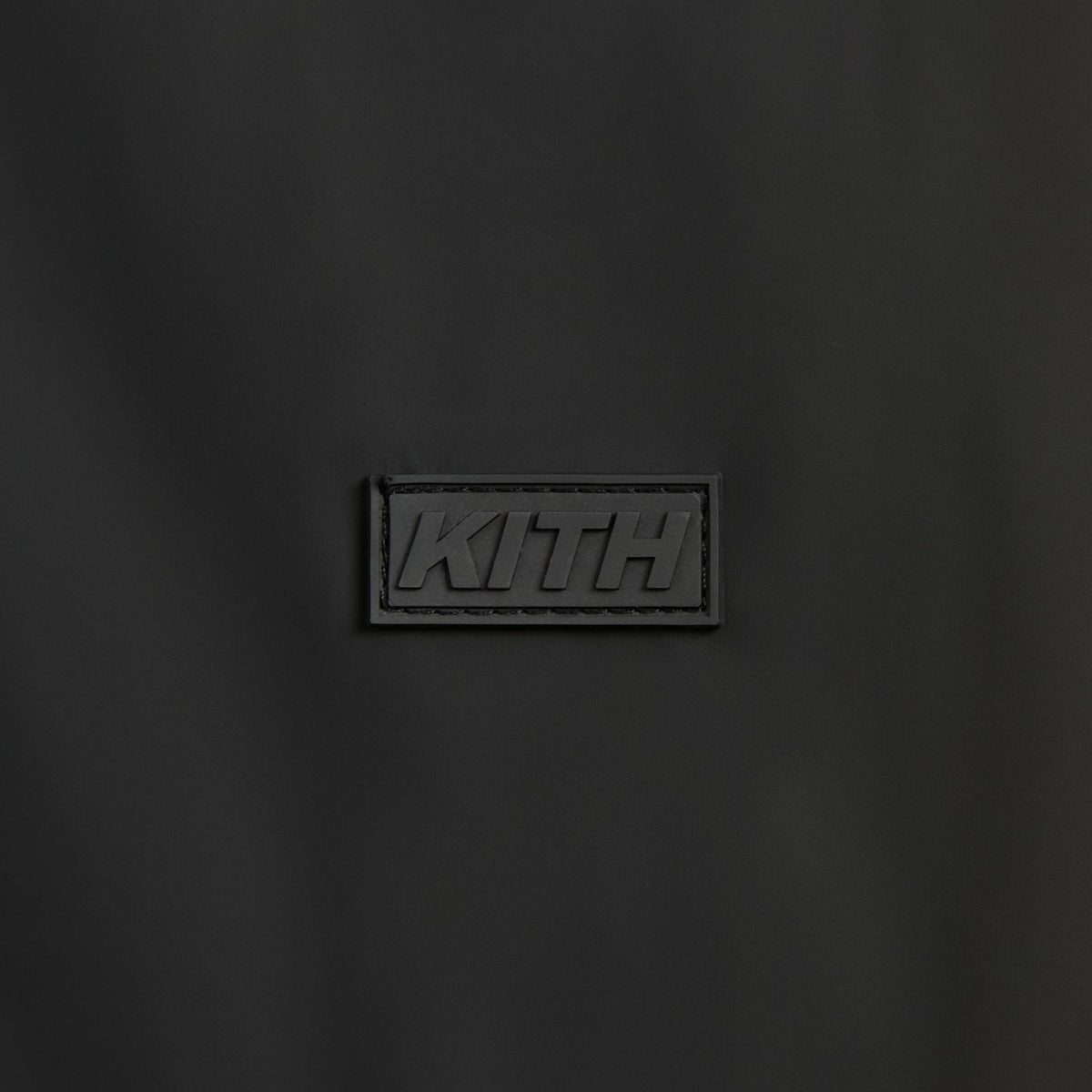 Kith Stretch Poly Brixton Shirt Jacket in black, close-up of rubberized Kith logo patch on chest