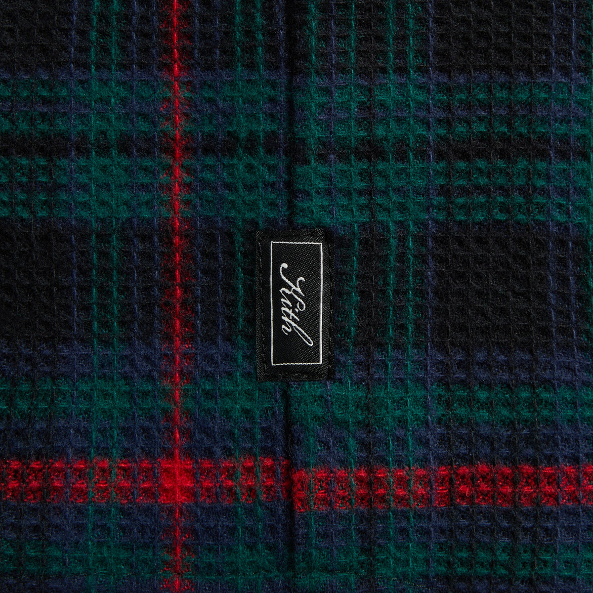 Close-up of the Kith woven label on the navy and green plaid Tomas shirt