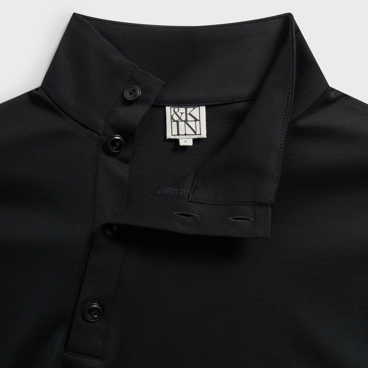 Close-up of the collar, snap placket and &Kin label on the black Interlock Cyrus mock-neck