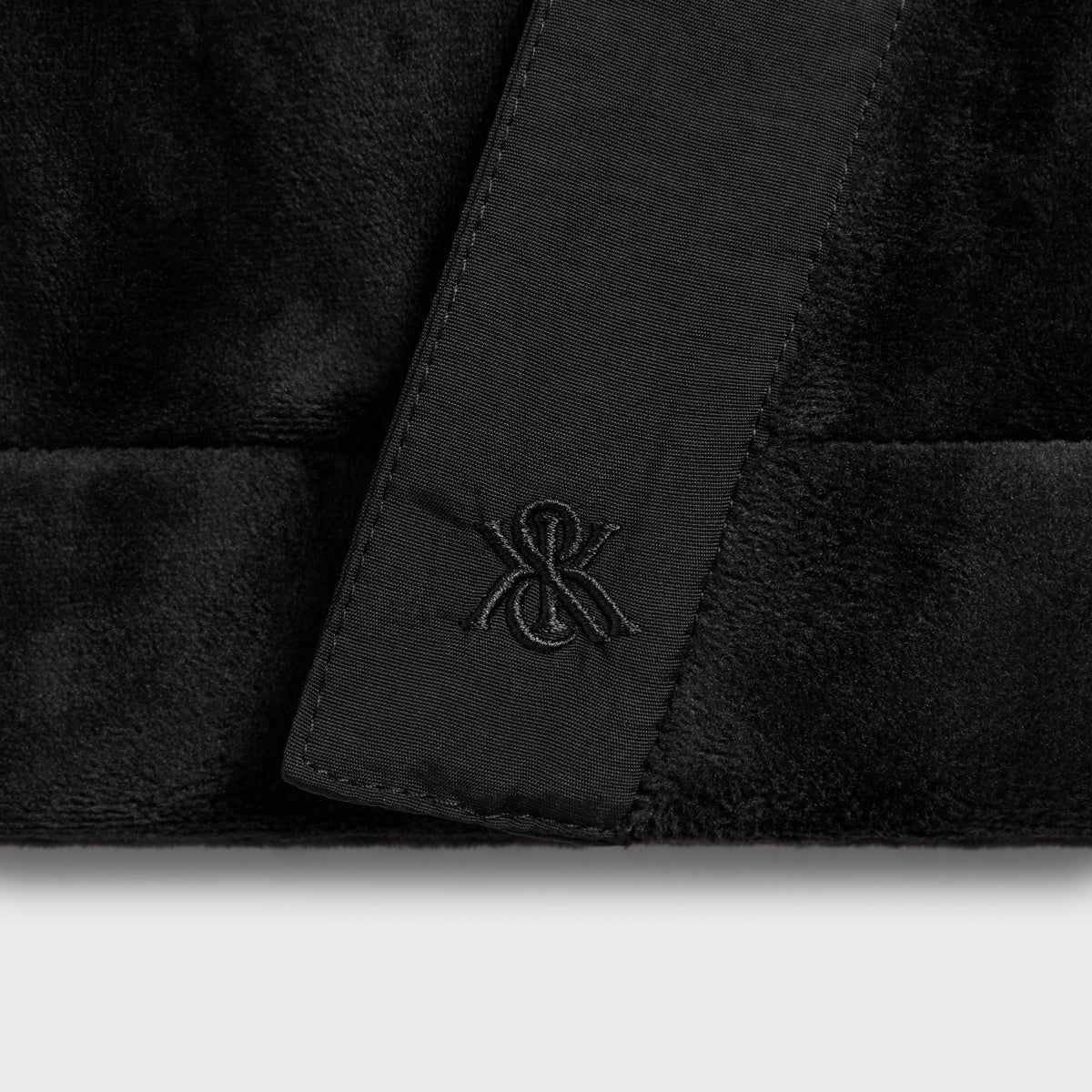Kith Plush Double Fleece Strauss Cardigan in black, close-up of wrap front trim with embroidered monogram on velvety fleece